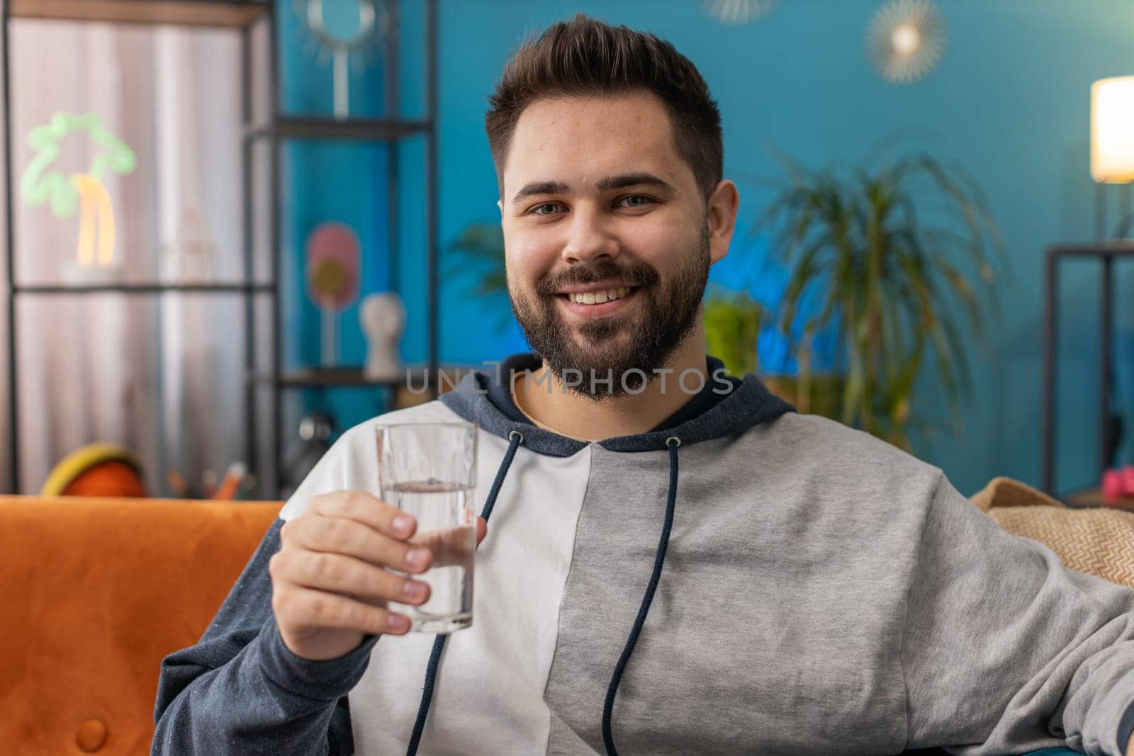 Thirsty man holding glass of natural aqua make sips drinking still water preventing dehydration sits at home living room. Caucasian guy with good life habits, healthy slimming, weight loss concept