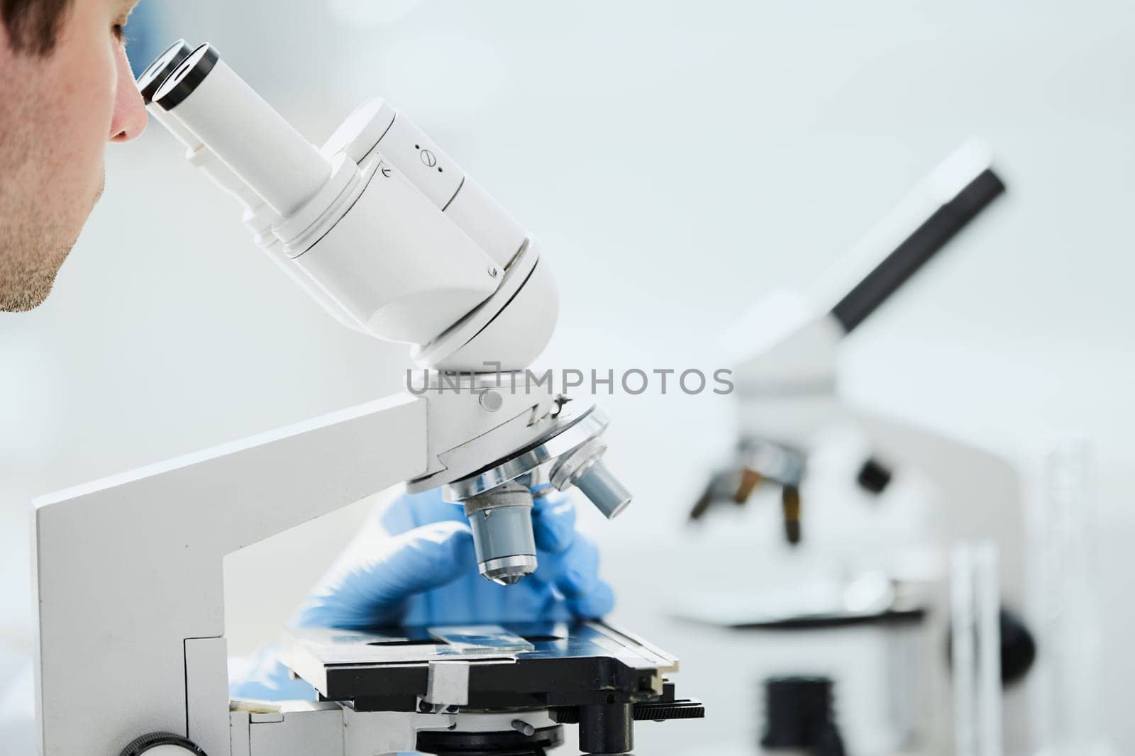 selective focus of male scientist looking through microscope in laboratory