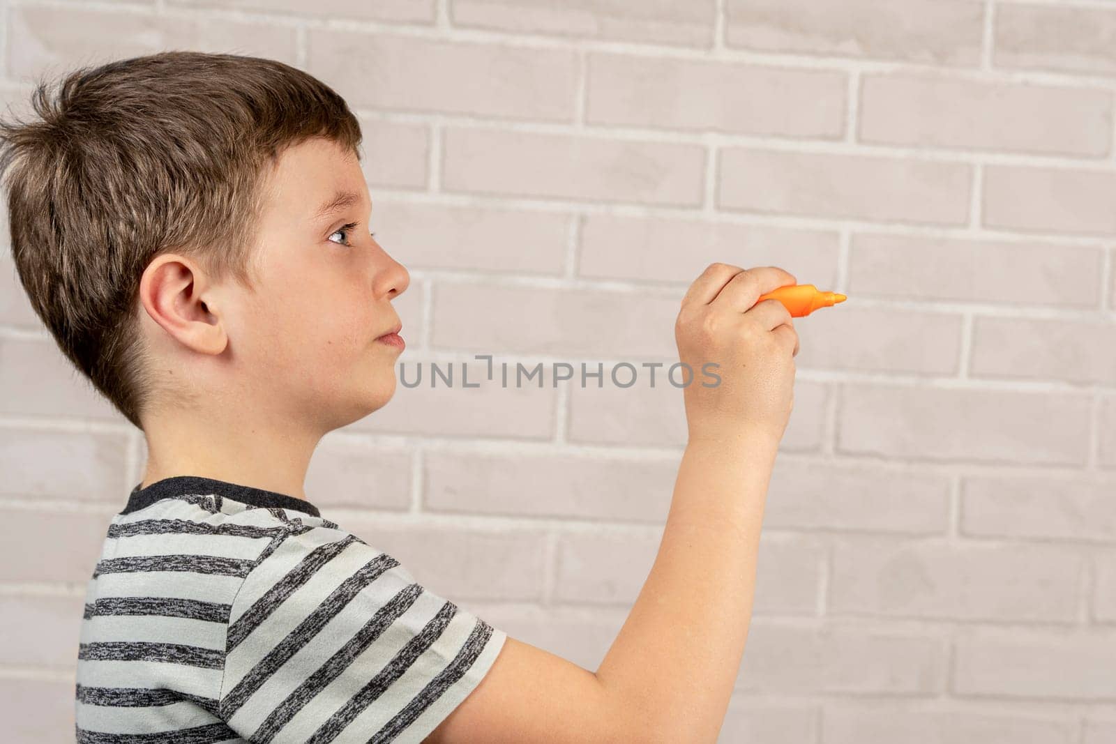 A happy Caucasian boy of school age writes in the air with an orange marker. The concept of study and school activities and education