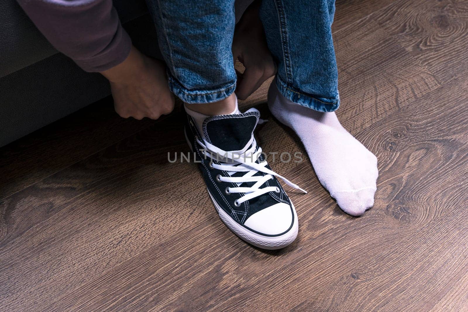 a teenage girl, sitting on the couch in one sneaker. there are no sneakers on my foot. blue jeans, sneakers and white socks. A fashionable concept in casual style. Choosing clothes