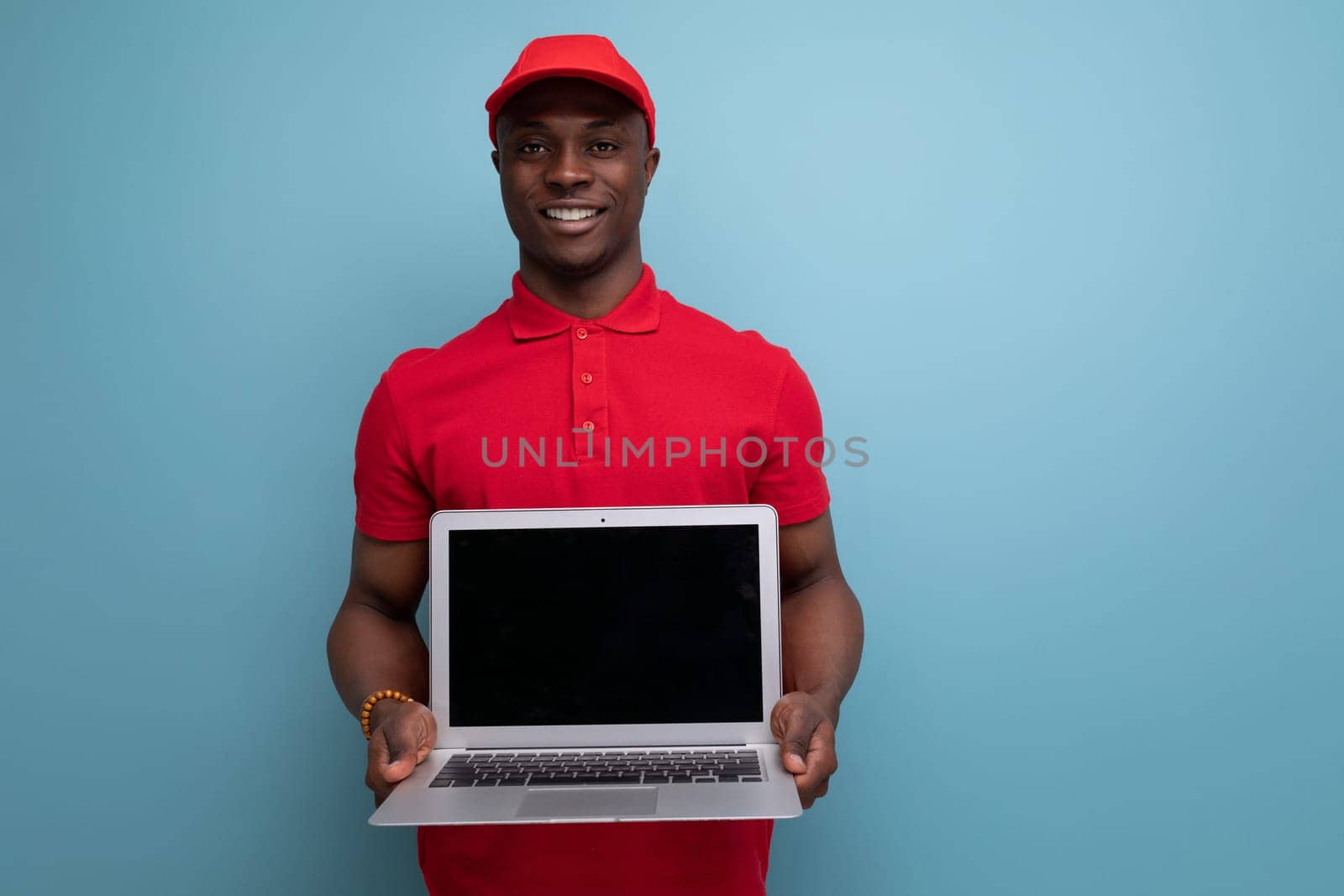 young delivery worker american man in red rendered t-shirt and caps showing advertisement on laptop with mockup.