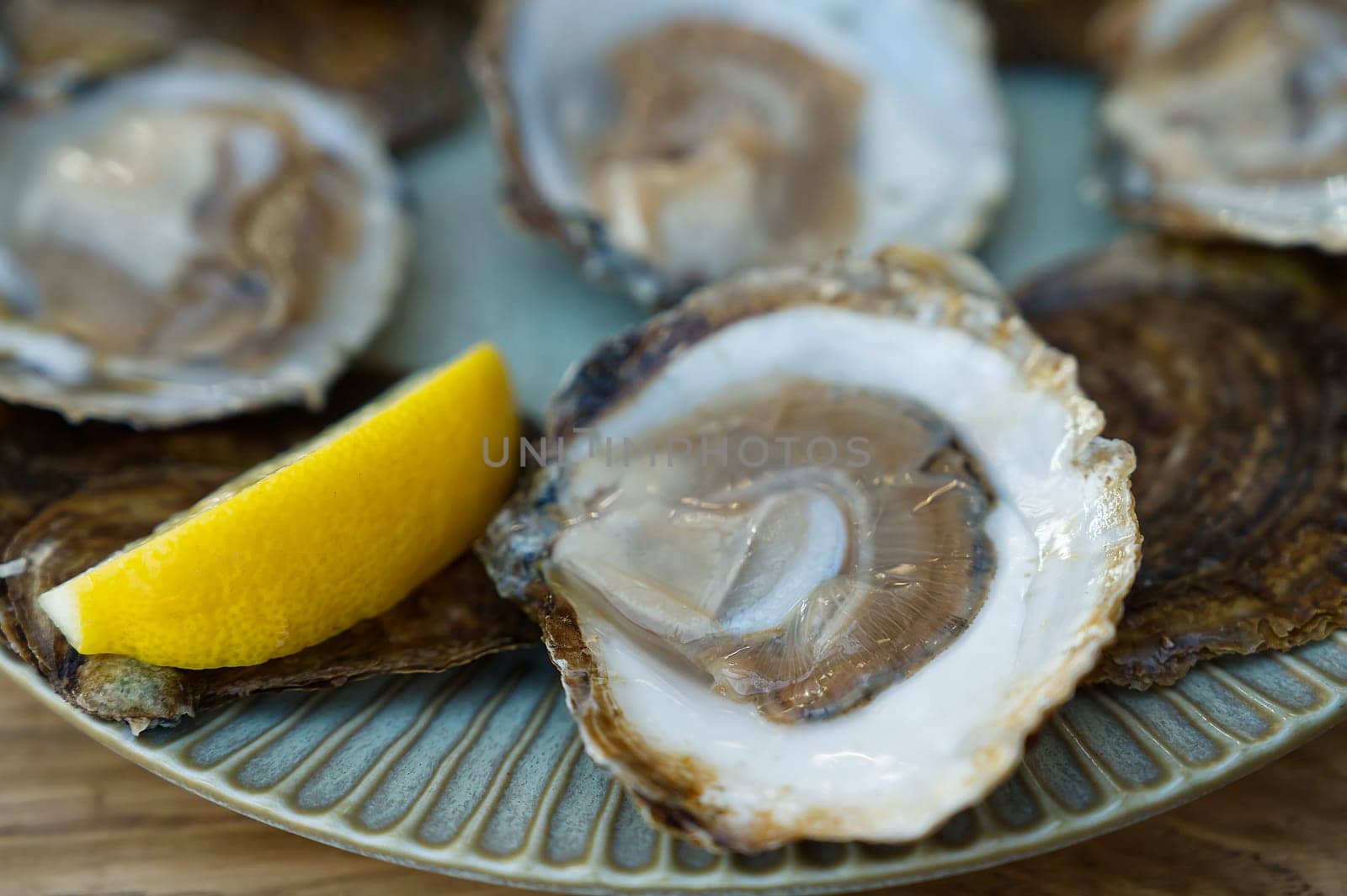 Fresh oysters served on a plate with lemon on old wooden table. Oysters served in fish restaurant by PhotoTime