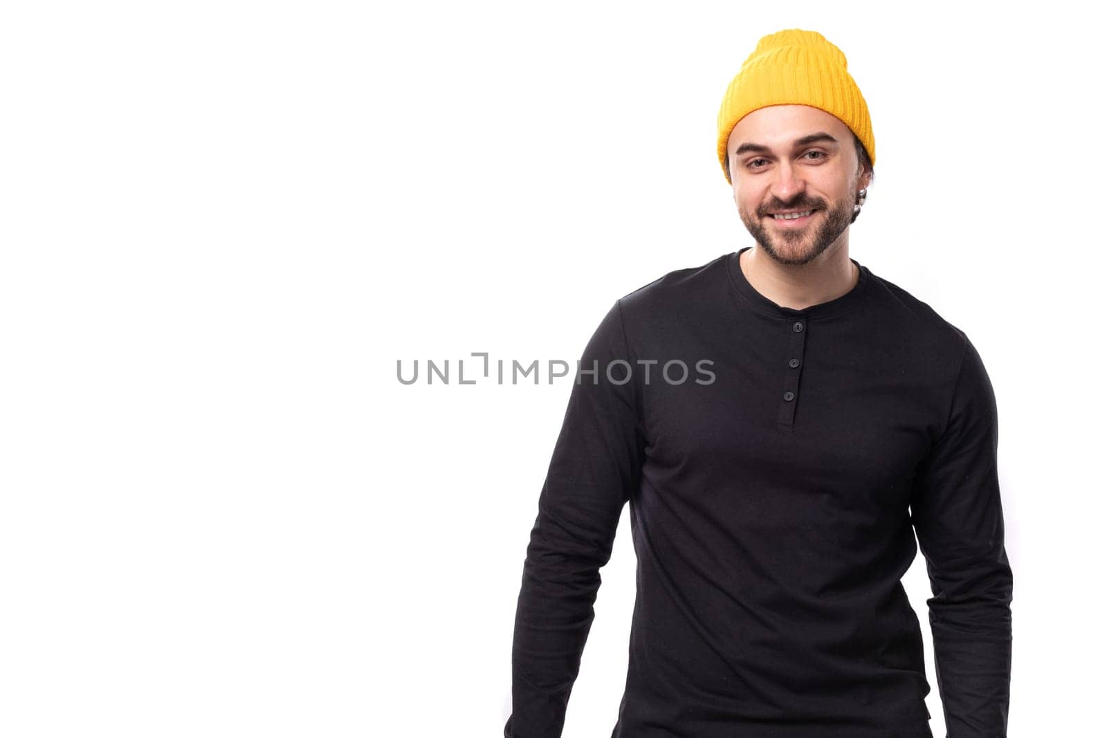 young brutal male model dressed in a black jacket and a yellow hat is smiling on a white background with copy space.