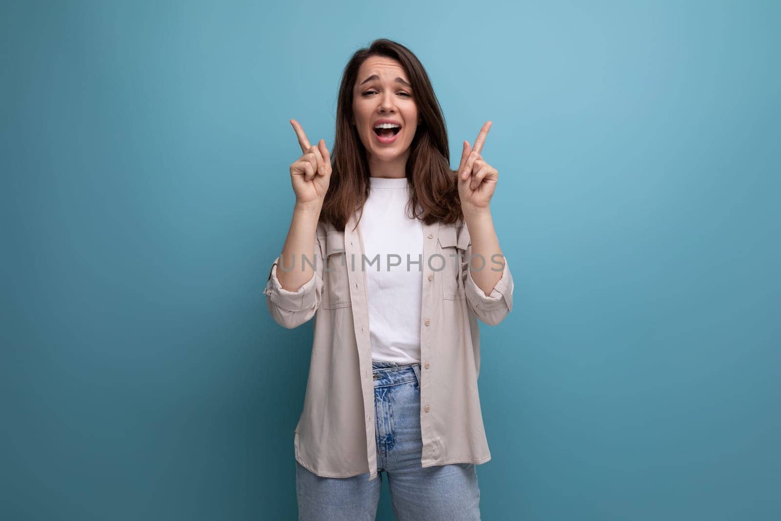 ecstatic 30s dark haired woman in beige shirt on blue background.