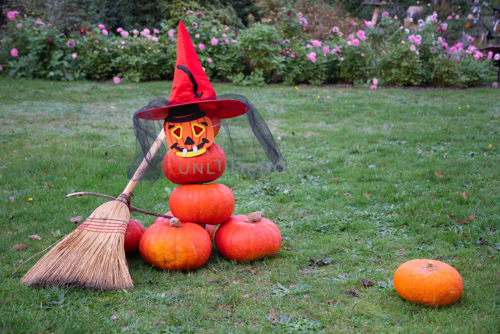 stacked pumpkin pyramid stuffed with halloween spooky ghost in hat and mask with broom garden decor. High quality photo