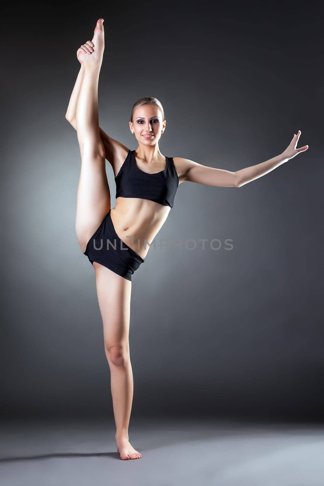 Smiling young woman posing on vertical splits in studio