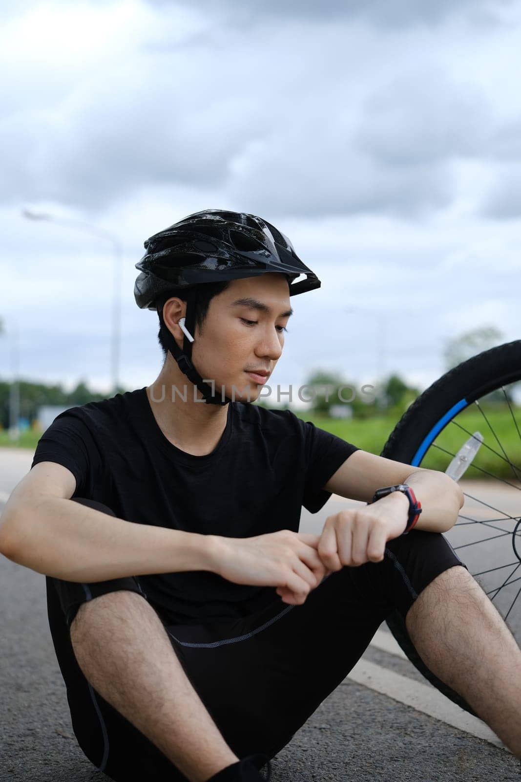 Young sportsman taking a break after riding bicycle and checking sport activity progress data on smartwatch by prathanchorruangsak