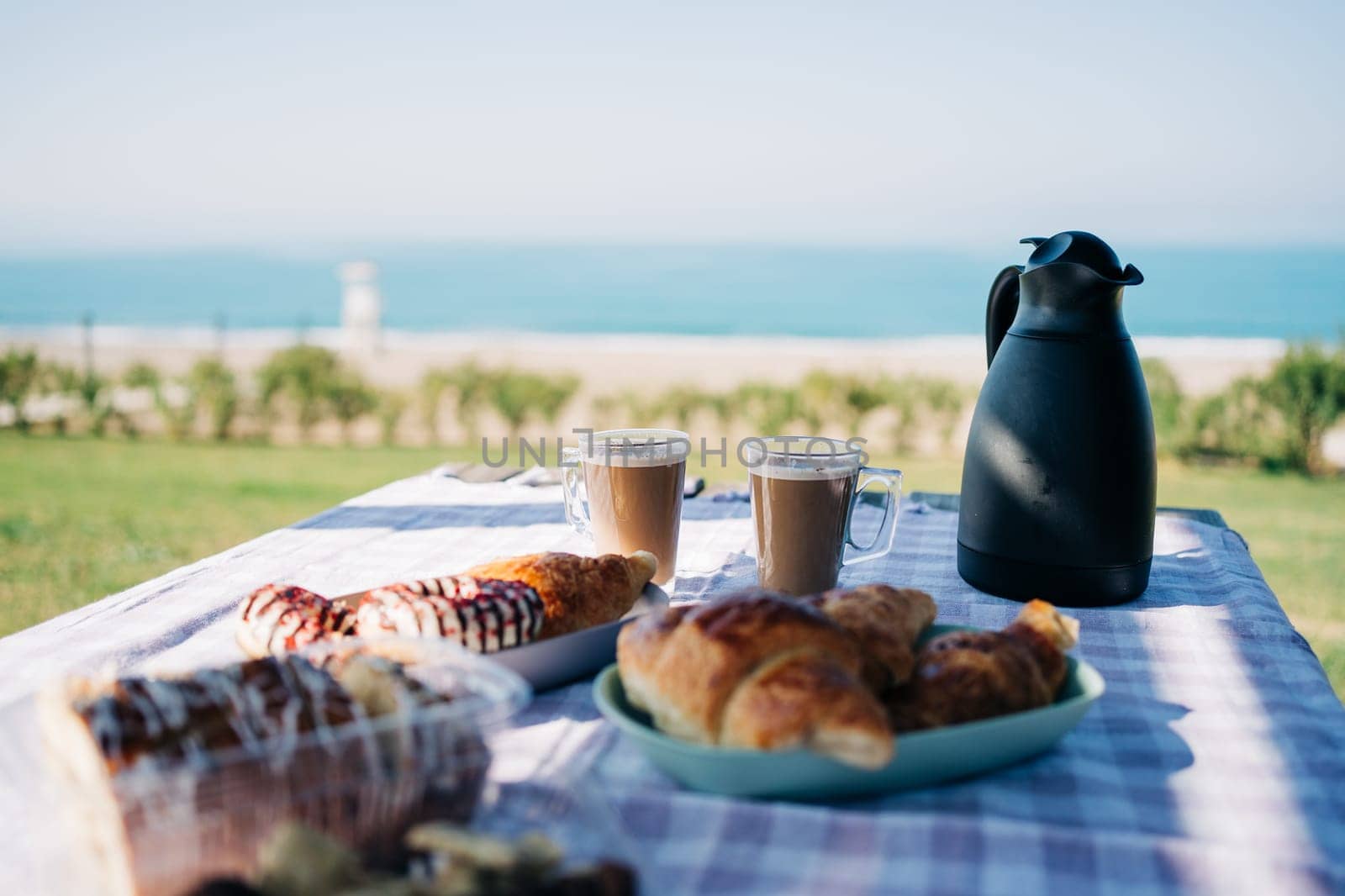 A picnic at the seaside beach. Breakfast with coffee, croissants and donuts by the ocean shore. by Ostanina