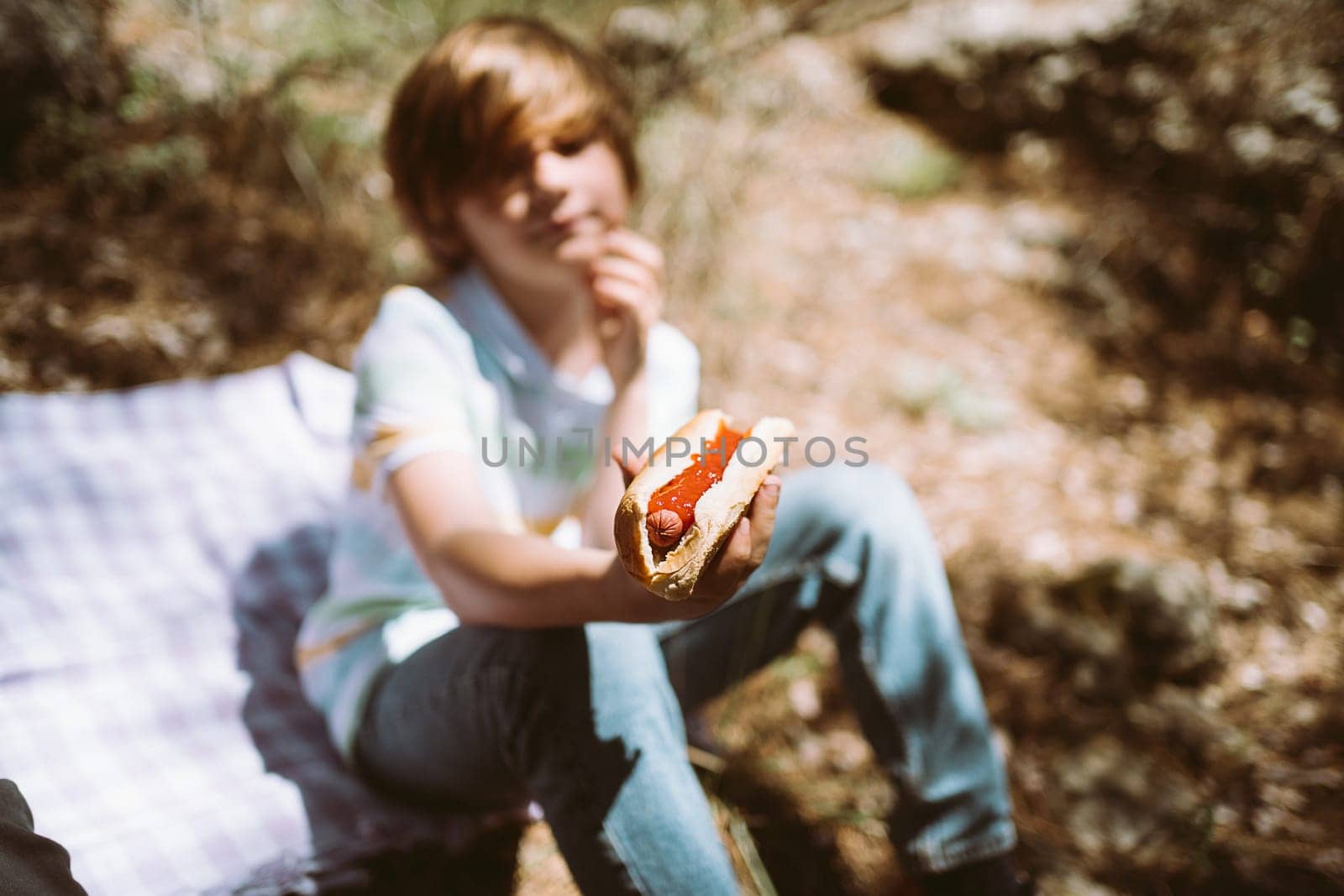 School boy kid child eating holding a juicy hotdog on a picnic outside in the city park