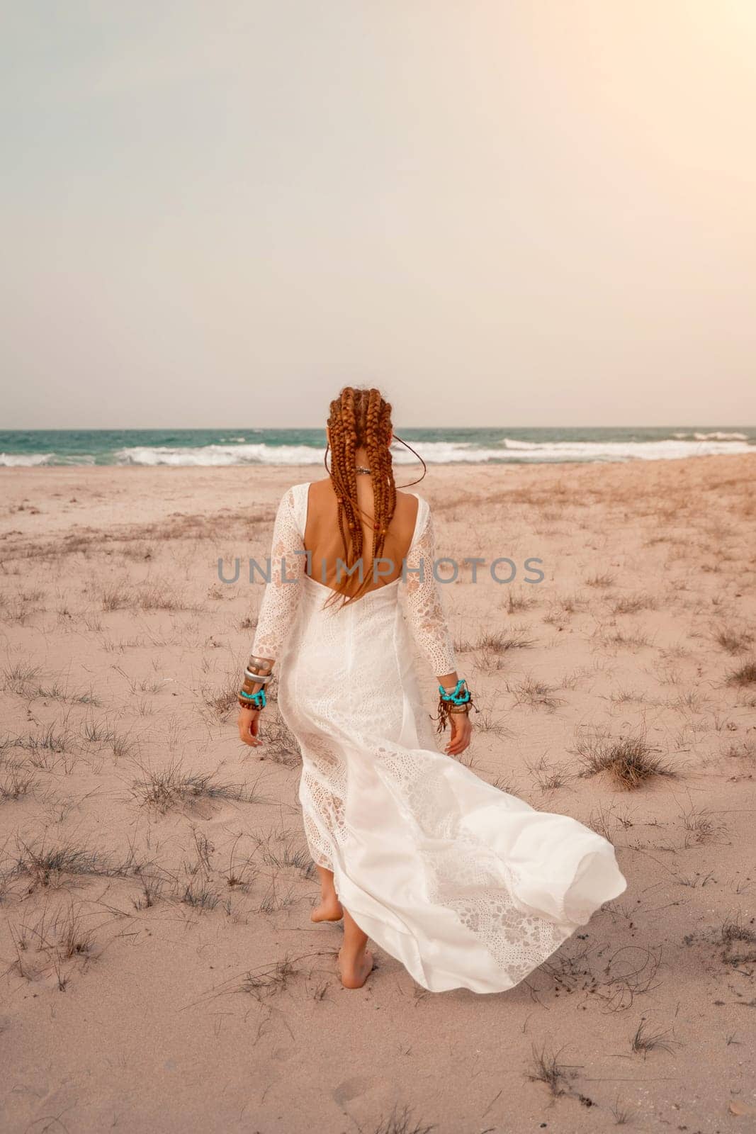 woman sea white dress. Model in boho style in a white long dress and silver jewelry on the beach. Her hair is braided, and there are many bracelets on her arms. by Matiunina