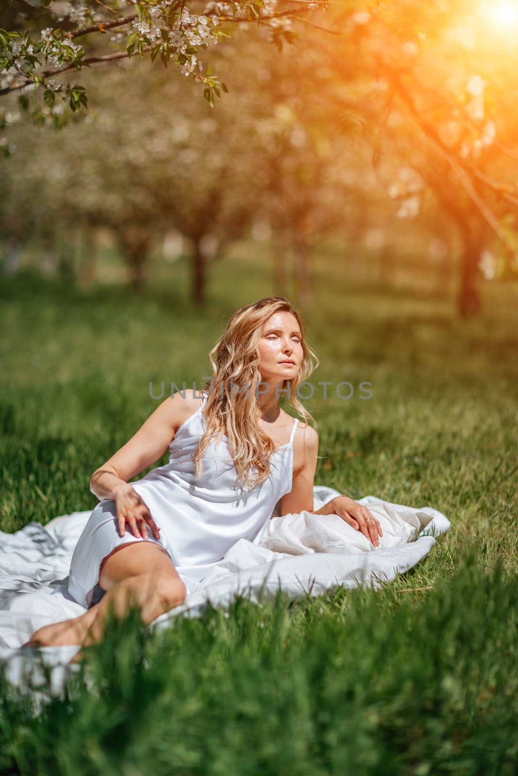 woman garden. she sleeps on a white bed in the fresh spring grass in the garden. Dressed in a blue nightgown
