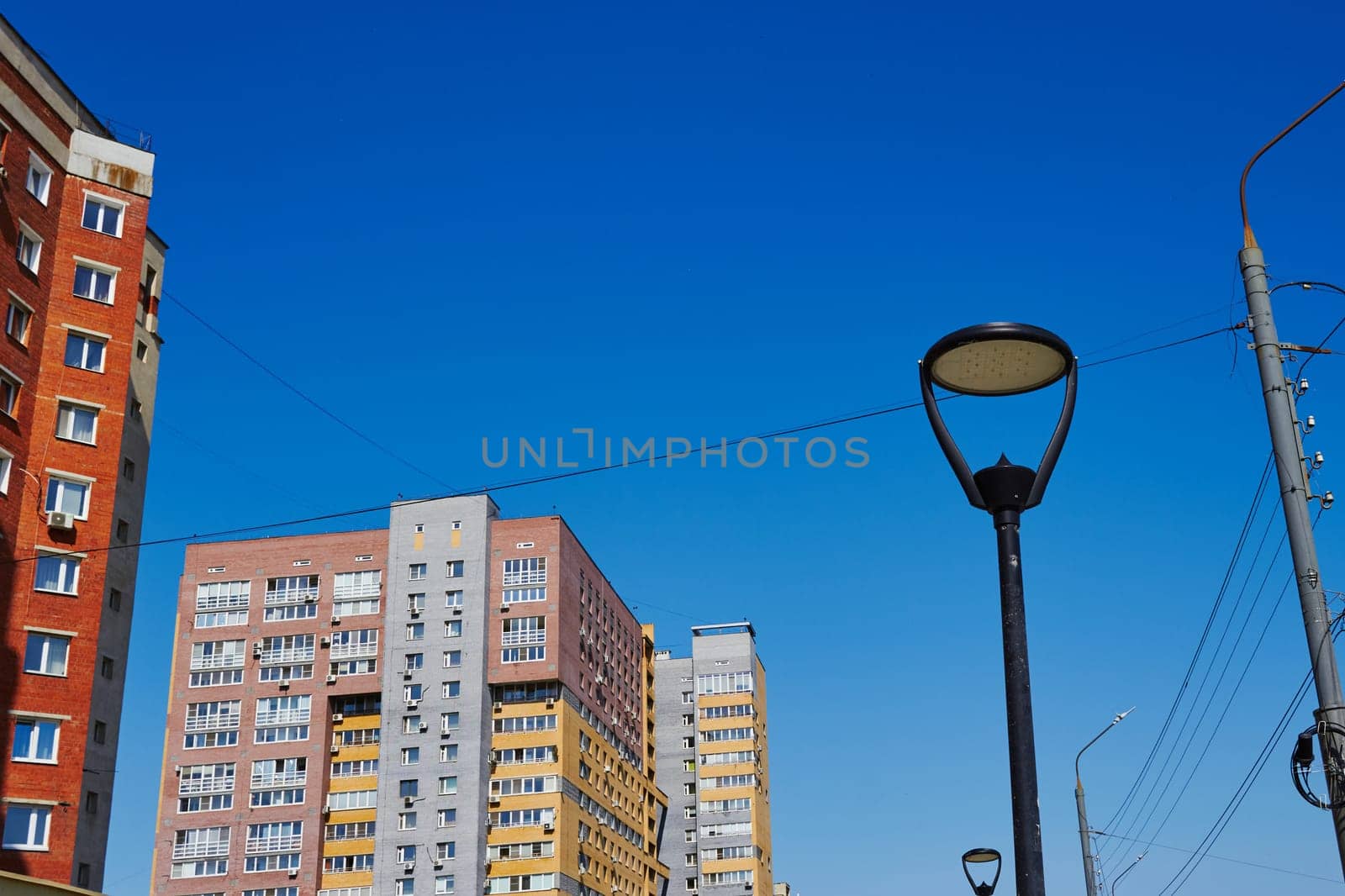 Photo of lamppost lighting and multi-storey residential buildings. Sunny day. Blue sky.