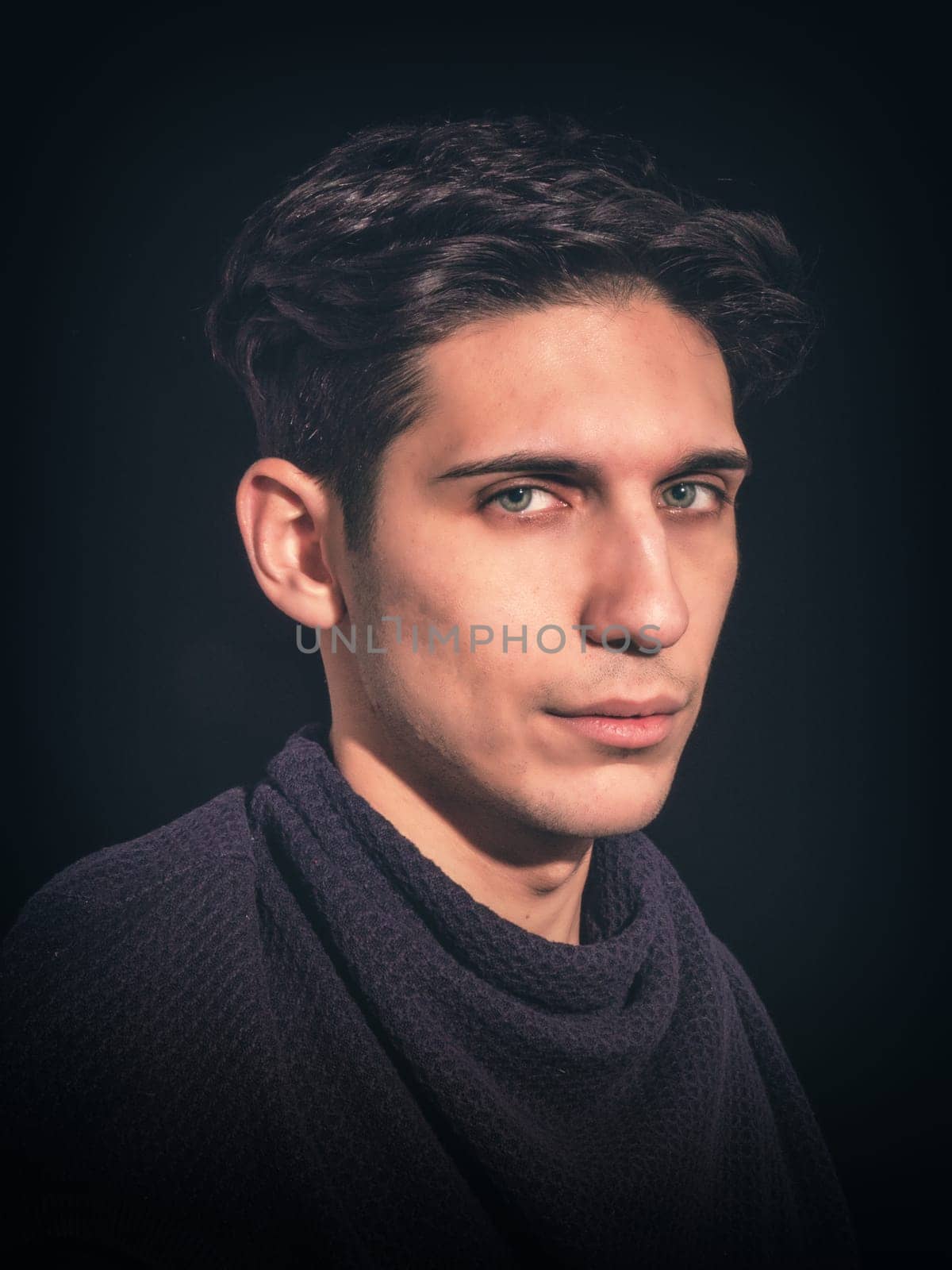 Closeup of handsome young man, dark hair and green eyes, on black background