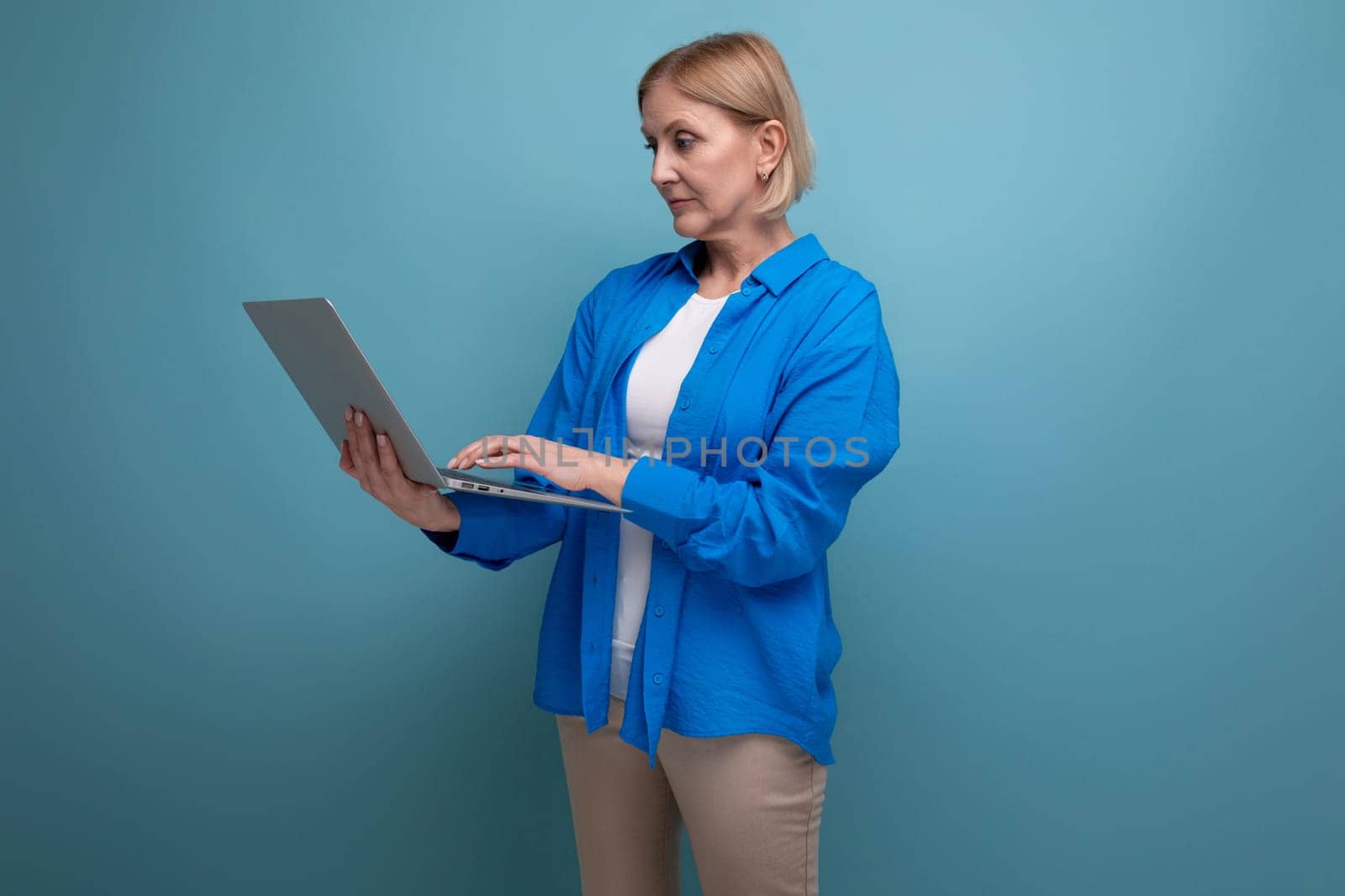 50s middle aged business woman working as freelancer with laptop on blue background with copy space.