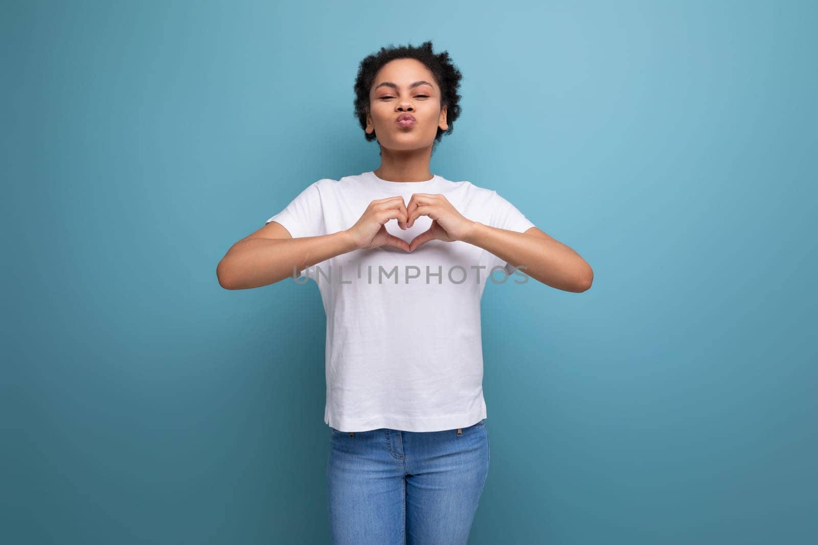 well-groomed beautiful young swarthy woman with fluffy curly hair dressed in a white t-shirt on a blue background with copy space.