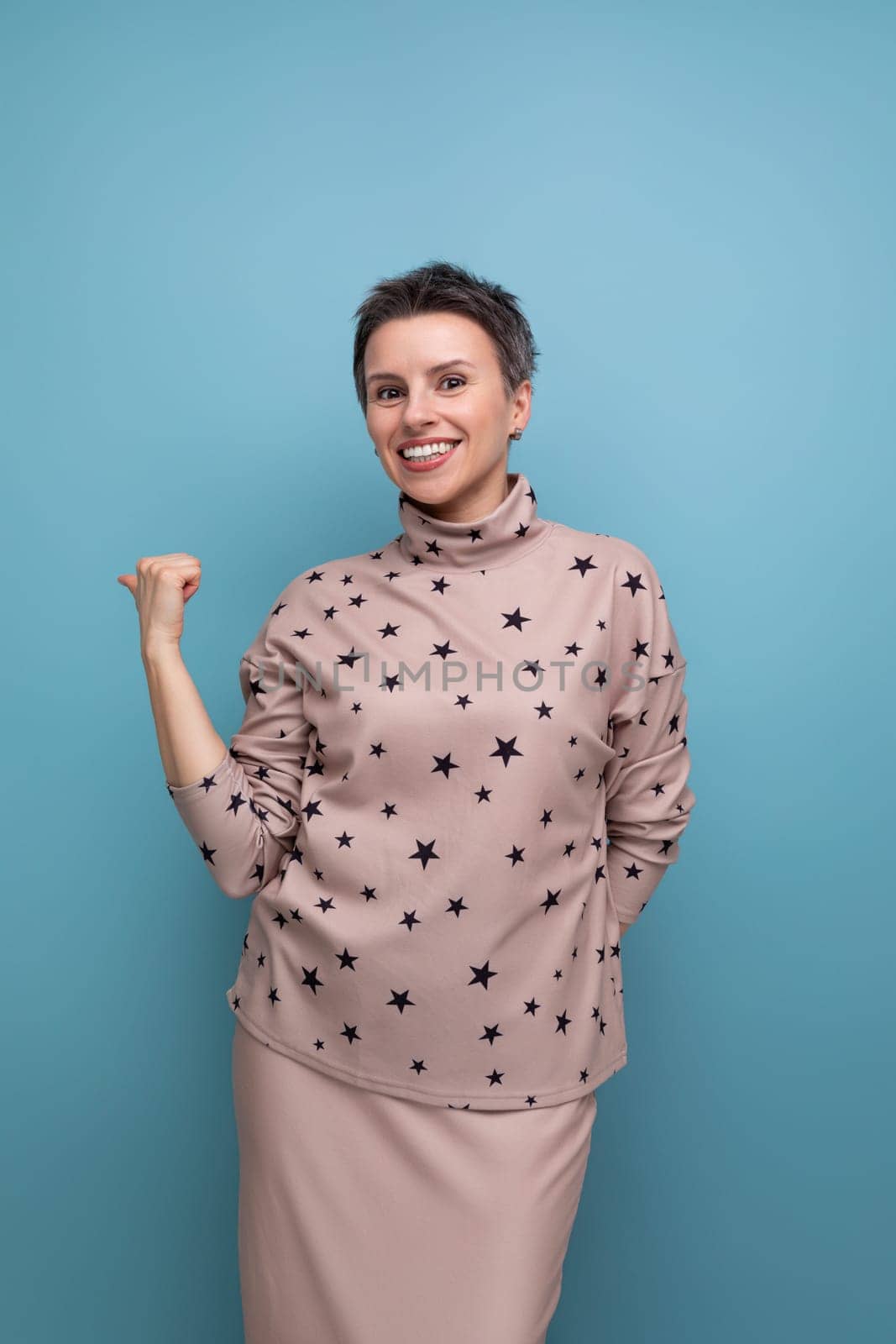 pretty caucasian young woman with a short haircut dressed in a beige suit points her finger to the side.