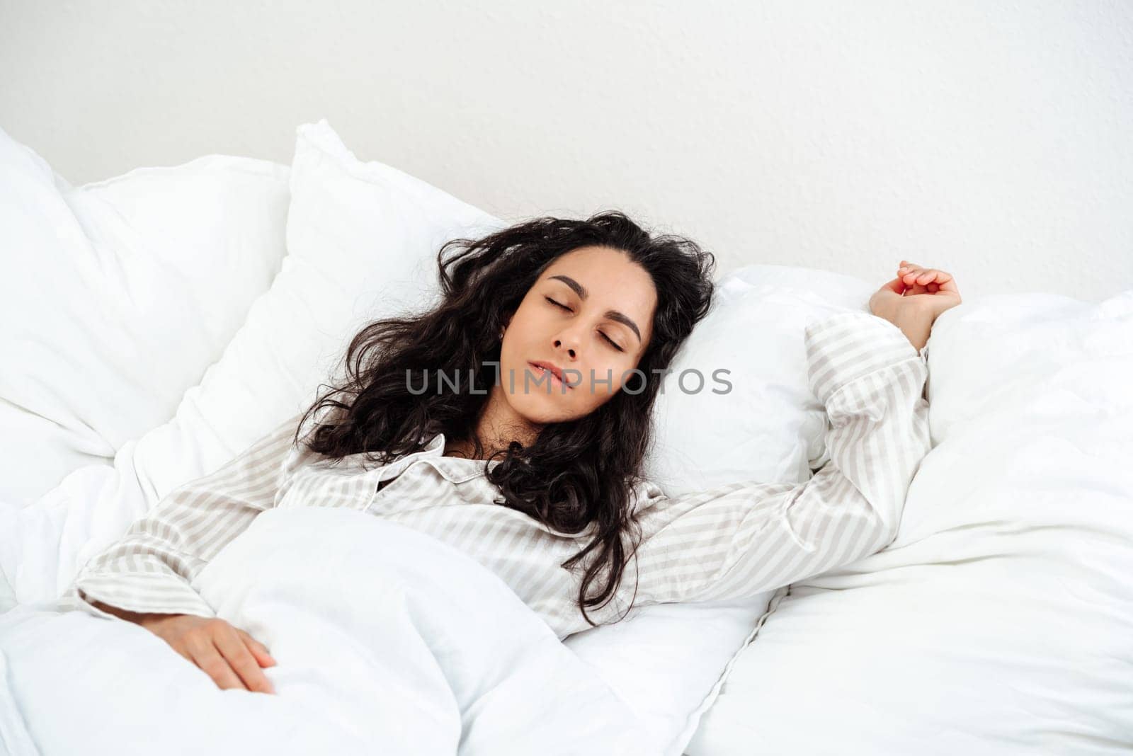 Peaceful serene beautiful young lady wear pajamas lying asleep relaxing sleeping in cozy white bed on soft pillow resting covered with blanket enjoying good healthy sleep concept, above top view