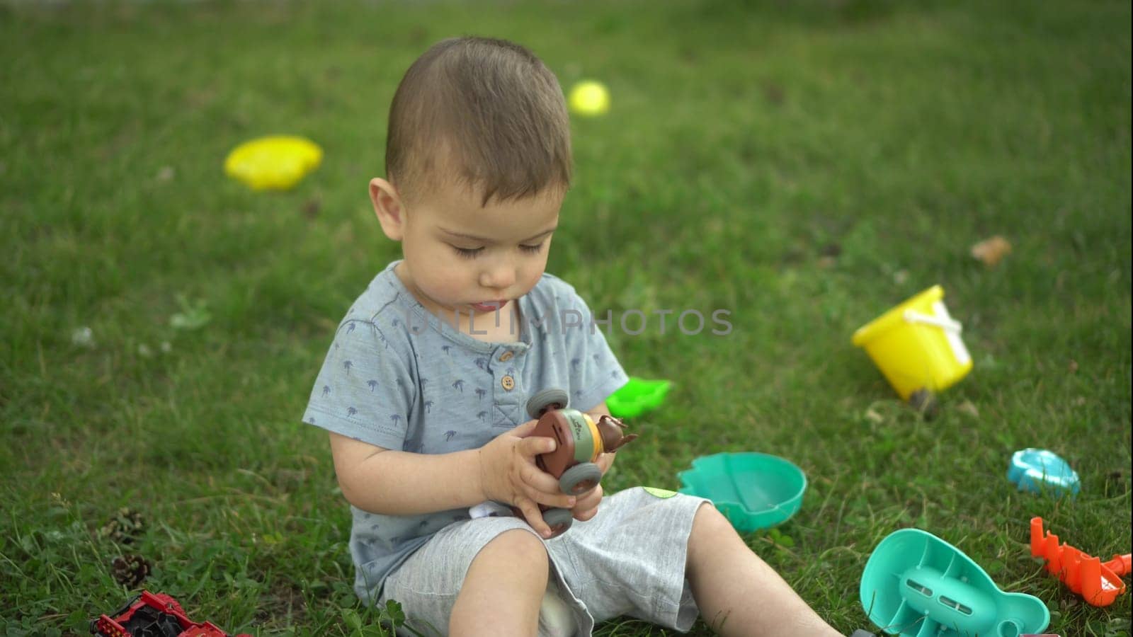 A one-year-old child sits on the grass and plays with toys. Little boy in the park. 4k