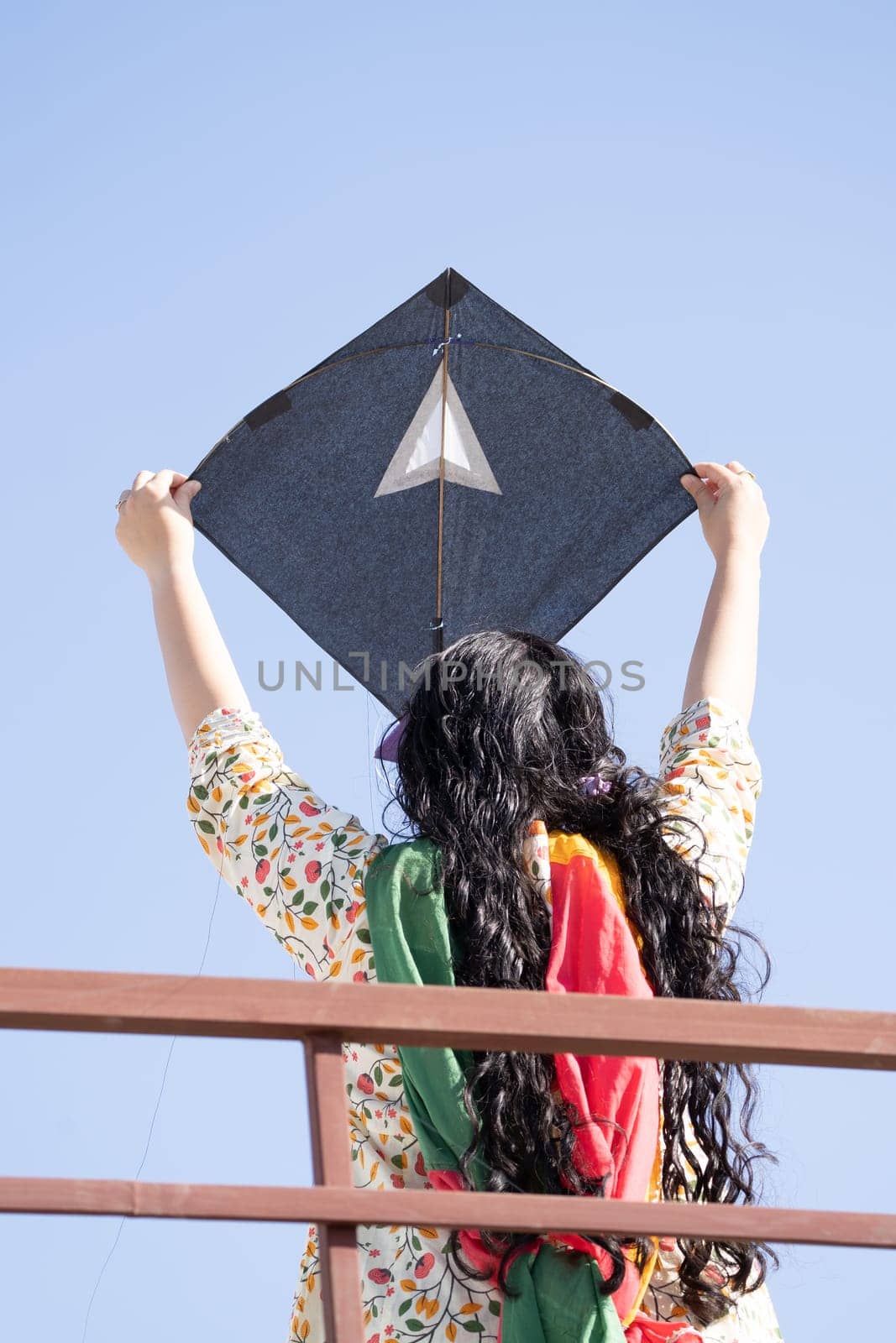Young girl in traditional indian clothing holding black kite high above head launching it on sankranti republic independence day celebrations by Shalinimathur