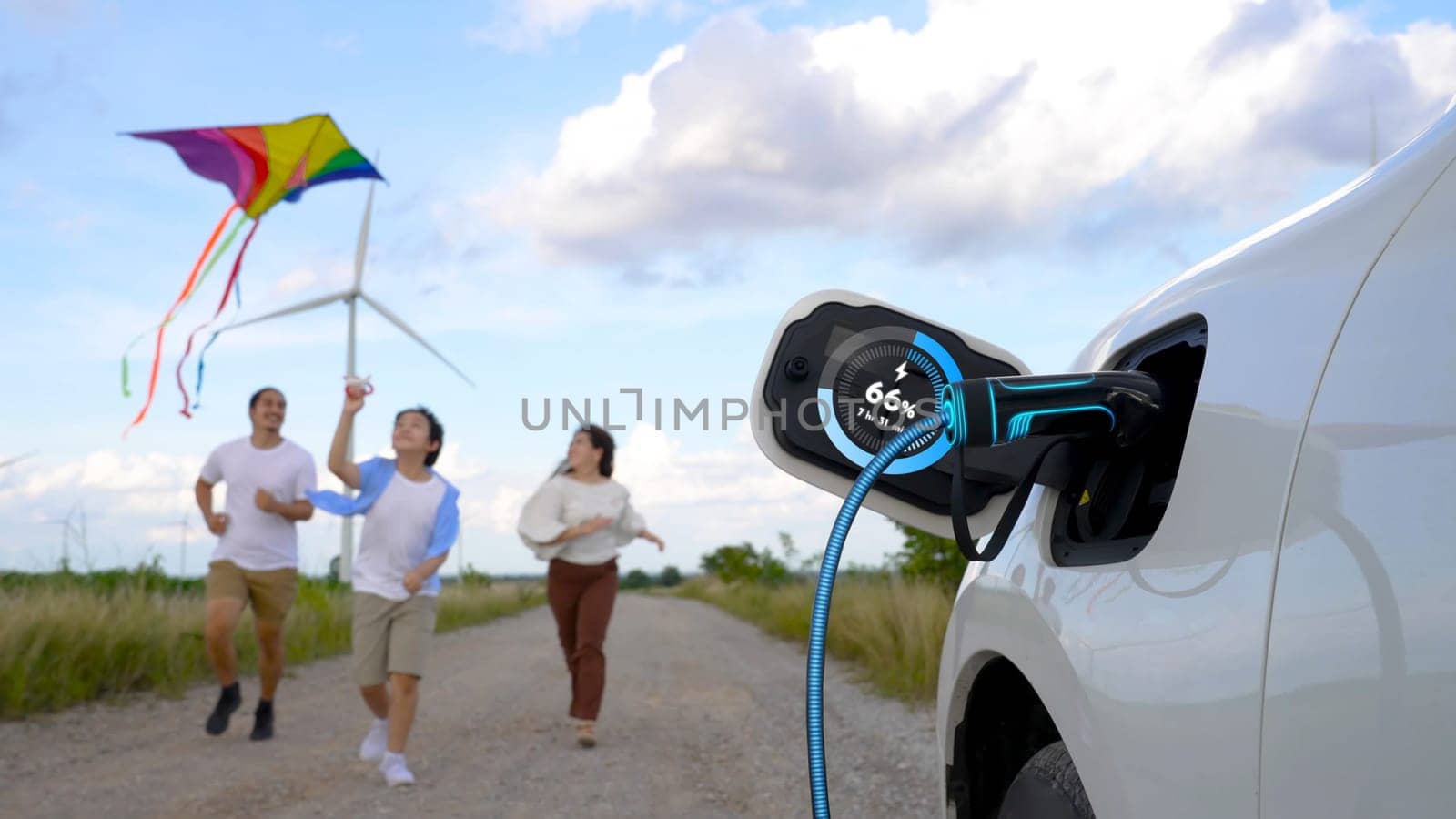 Focus eco-friendly EV car recharging display battery status hologram, charging station using eco-friendly energy wind turbine generator with happy family playing kite together in background. Peruse
