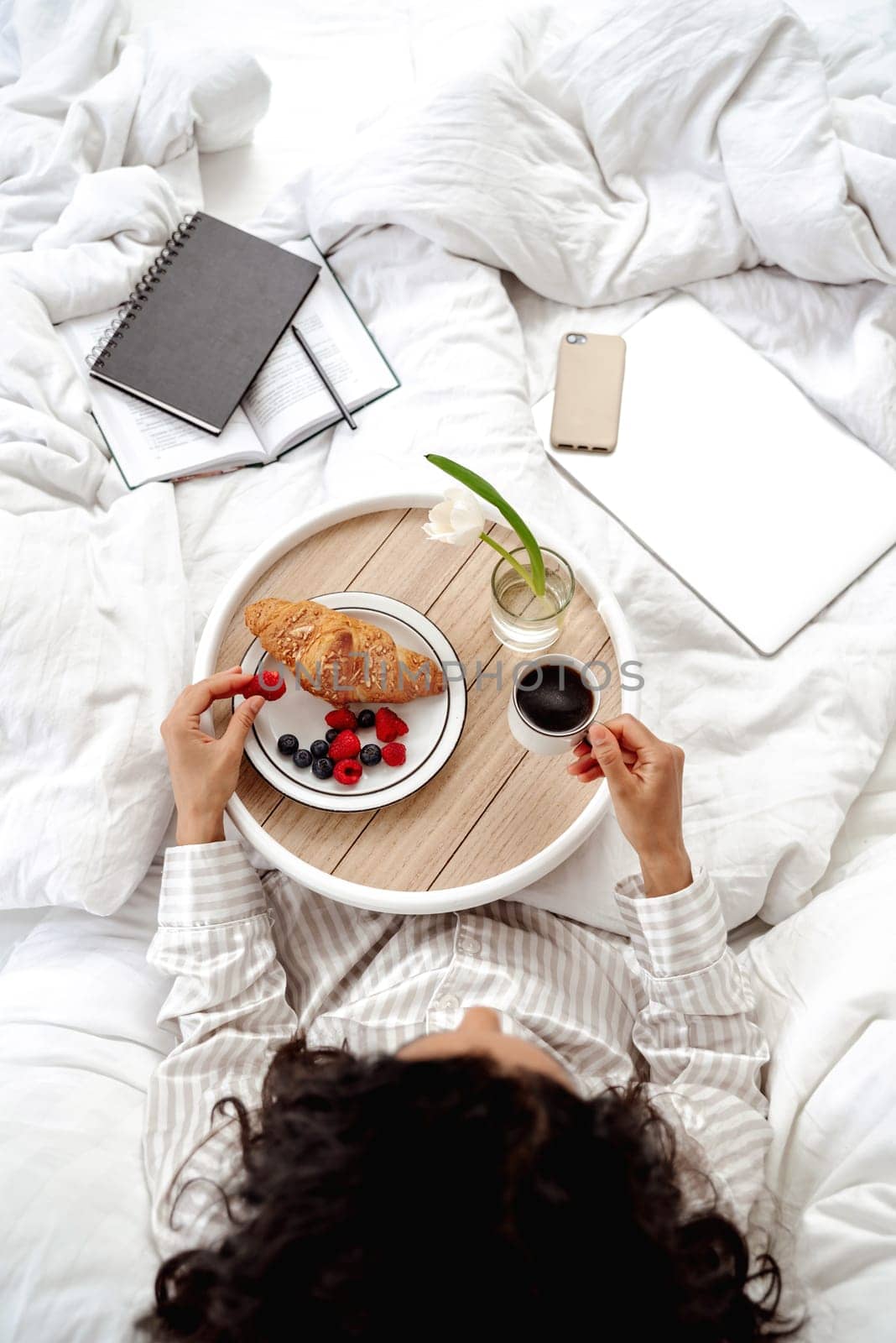 Top view aesthetics of morning and breakfast in bed. Woman going to eat berry and croissant. The girl organized the workspace and starts her morning with a productive working day