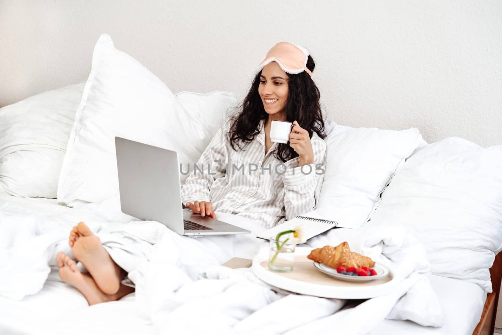 Young woman drink coffee and using a laptop. The girl just woke up and is looking through the mail at breakfast. Starting the working day in pleasure and comfort. Freelance blogger in a hotel room
