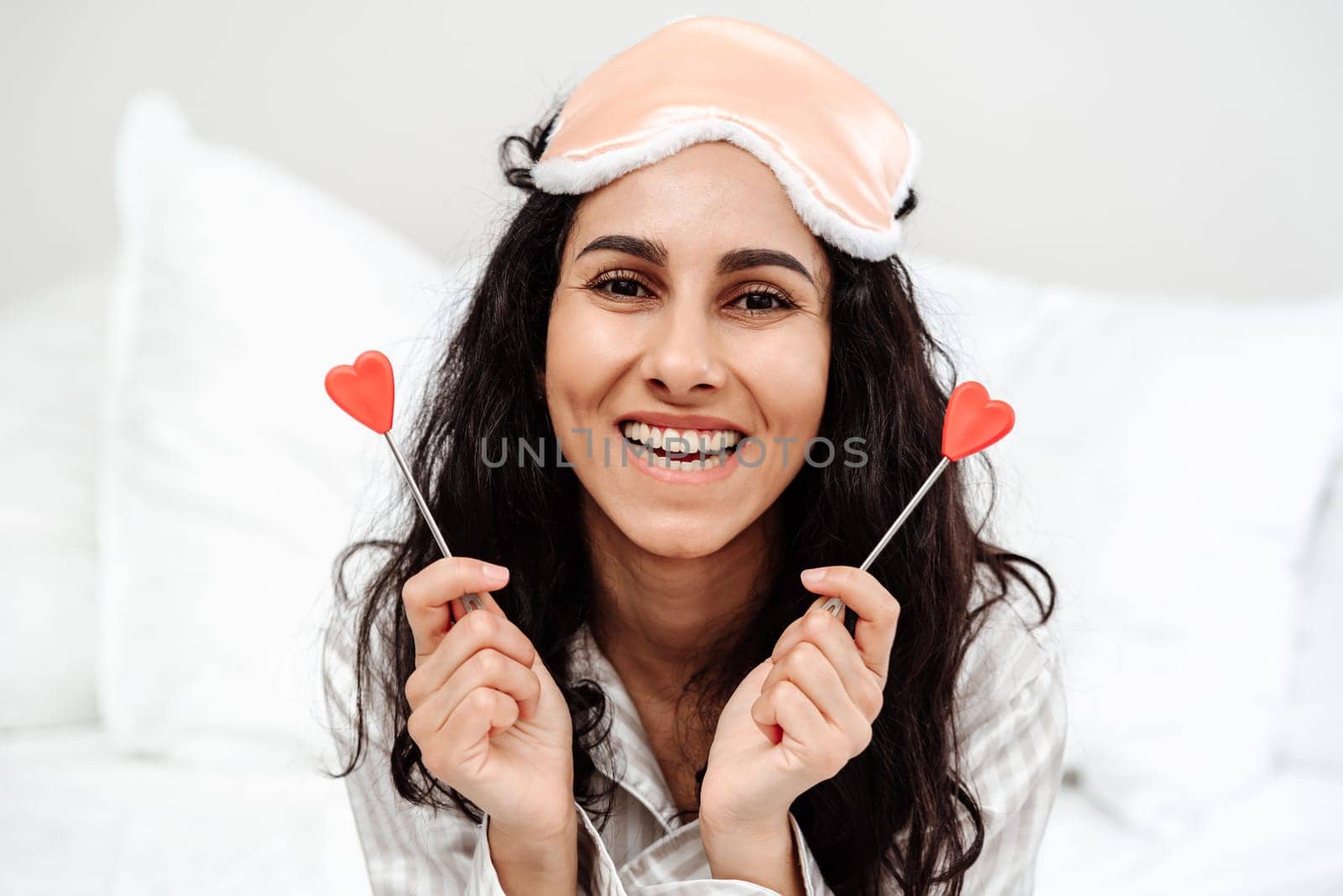 Portrait photo of a beautiful young woman of Arab appearance. The girl holds two hearts in her hands and smiles broadly looking in front of her. She just woke up in her bed and is ready for a holiday and a day off in love and joy