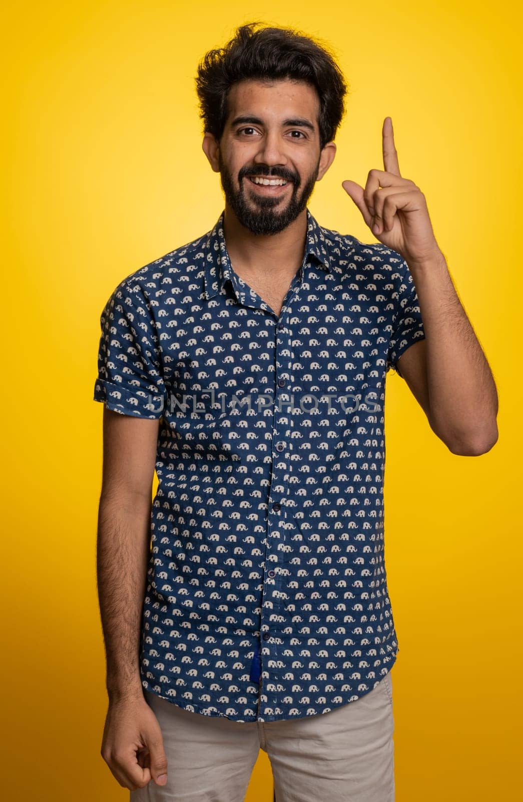 Eureka. Inspired young indian man pointing finger up with open mouth, having good idea, plan, startup, showing inspiration motivation gesture, problem solution. Bearded hindu guy on yellow background