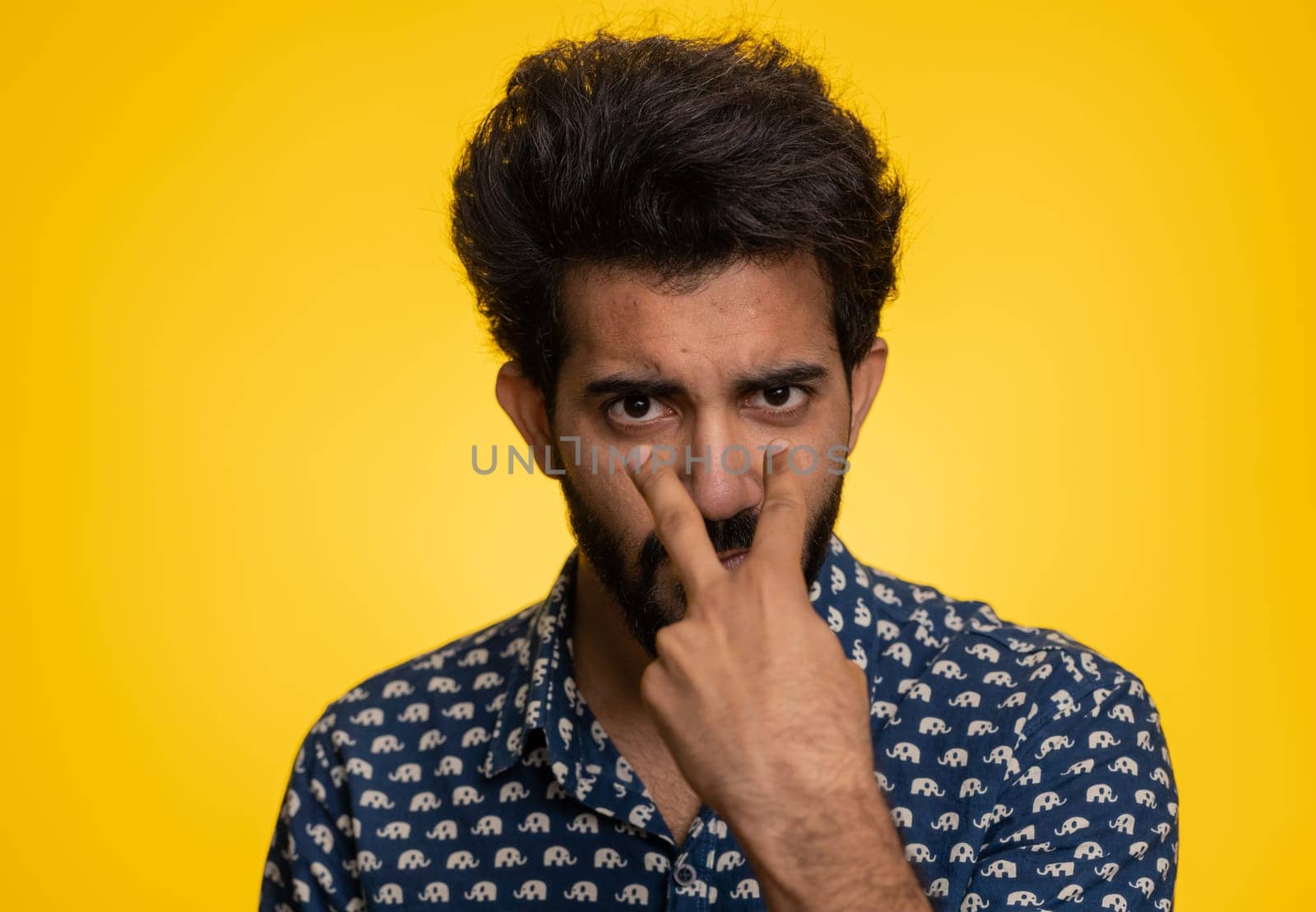 I am watching you. Young confident indian man pointing at his eyes and camera, show I am watching you gesture, spying on someone. Handsome bearded hindu guy isolated alone on yellow studio background