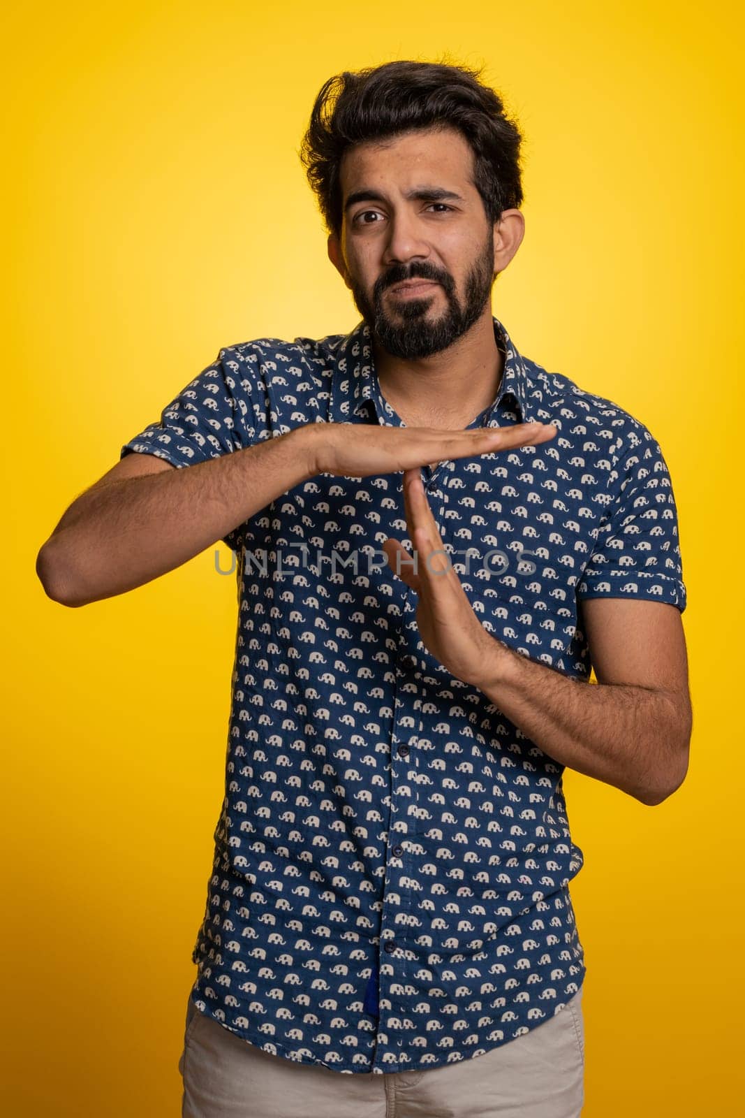 Tired serious upset young indian man showing time out gesture, limit or stop sign, no pressure, I need more time, relax, break, deadline. Handsome hindu guy isolated on studio yellow background indoor