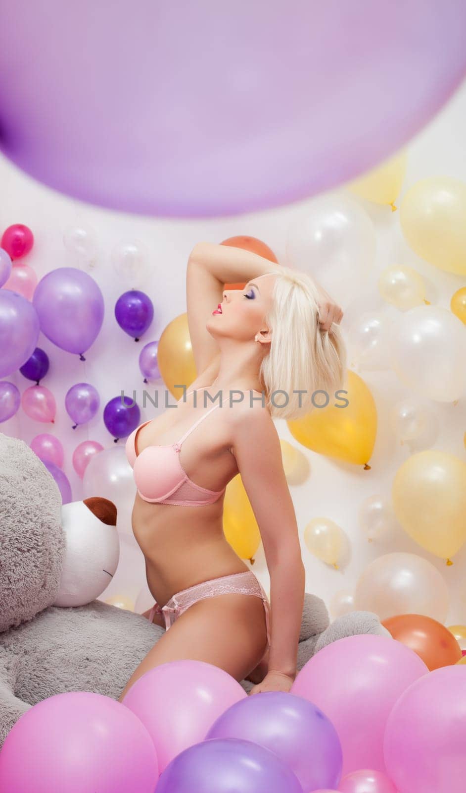 Seductive platinum blonde posing with balloons and teddy bear