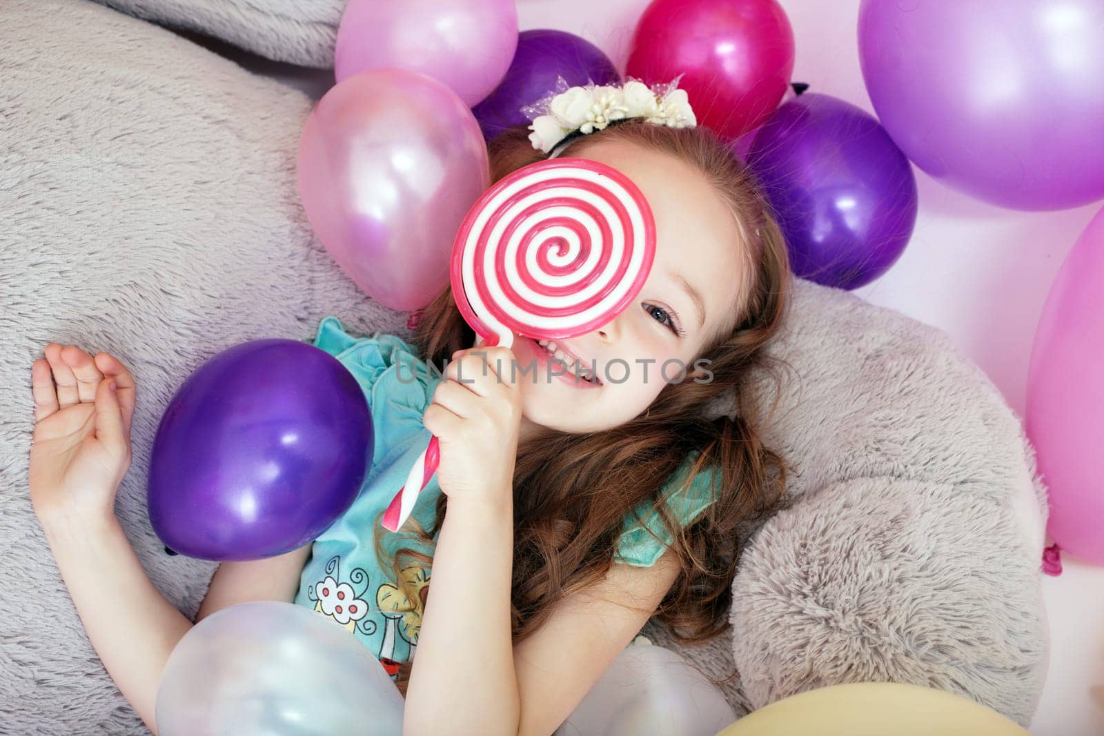 Playful curly girl hiding behind lollipop, close-up
