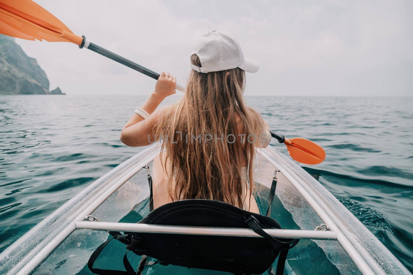 Woman in kayak back view. Happy young woman with long hair floating in transparent kayak on the crystal clear sea. Summer holiday vacation and cheerful female people having fun on the boat.