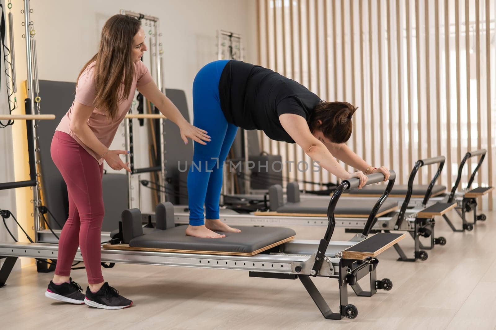 Overweight caucasian woman doing pilates exercises on reformer with personal trainer