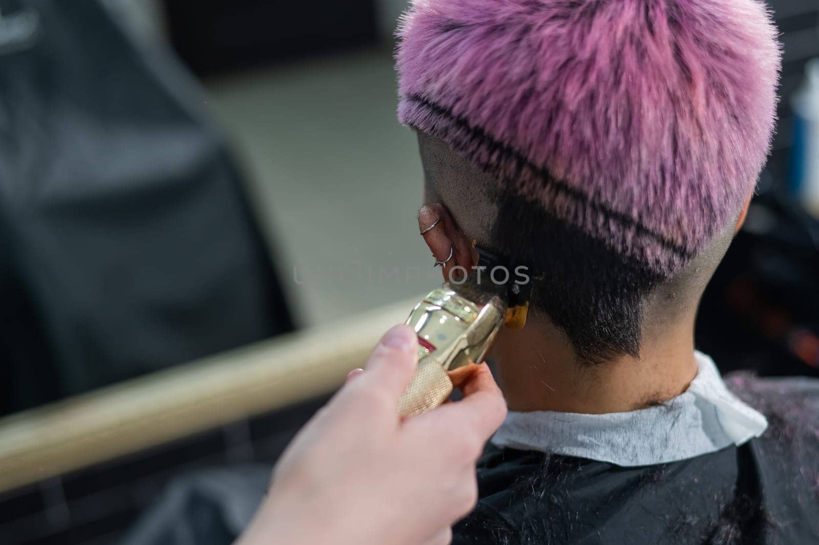 The hairdresser shaves the temple of a female client. Rear view of a woman with short pink hair in a barbershop. by mrwed54