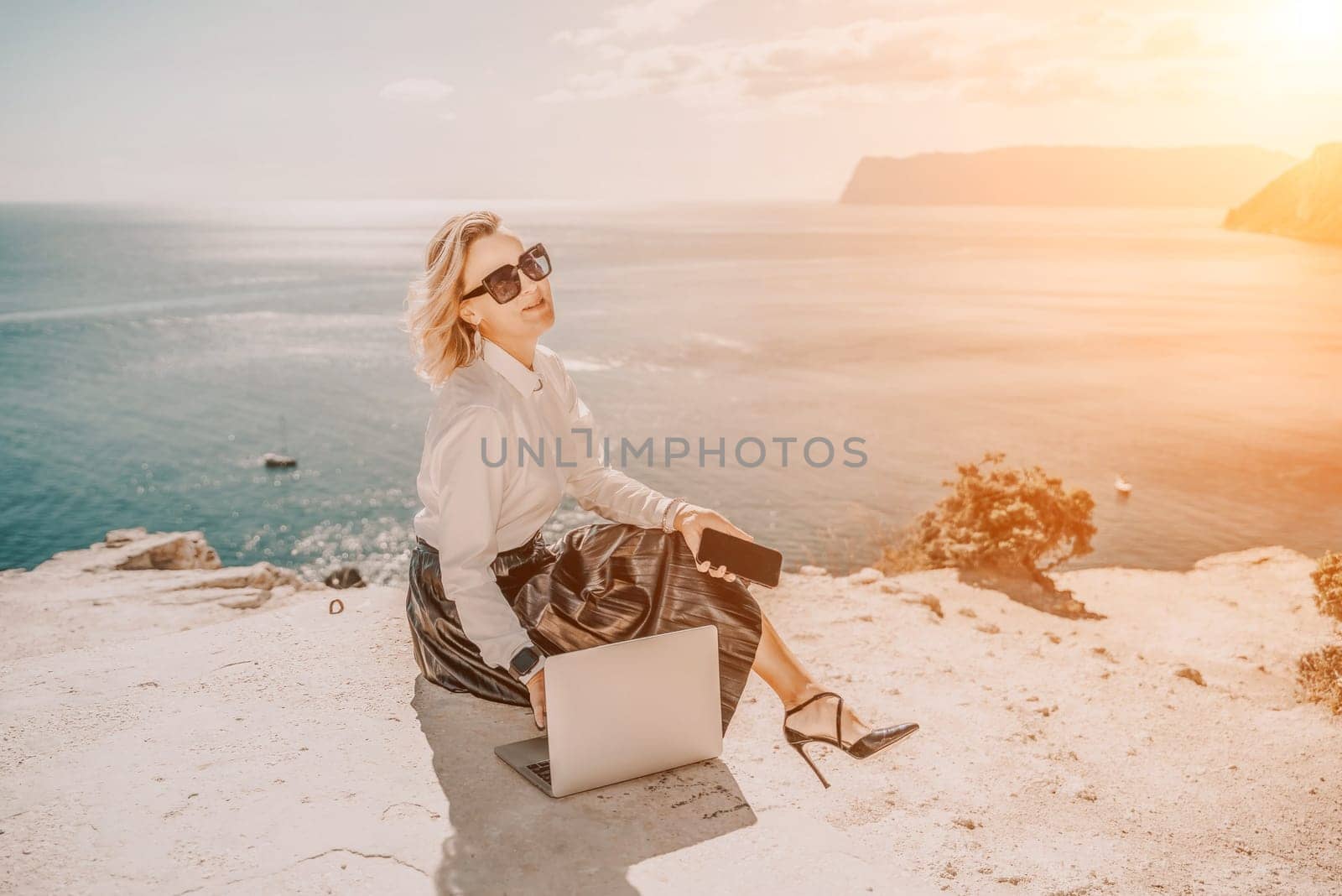 Freelance women sea. She is working on the computer. Good looking middle aged woman typing on a laptop keyboard outdoors with a beautiful sea view. The concept of remote work