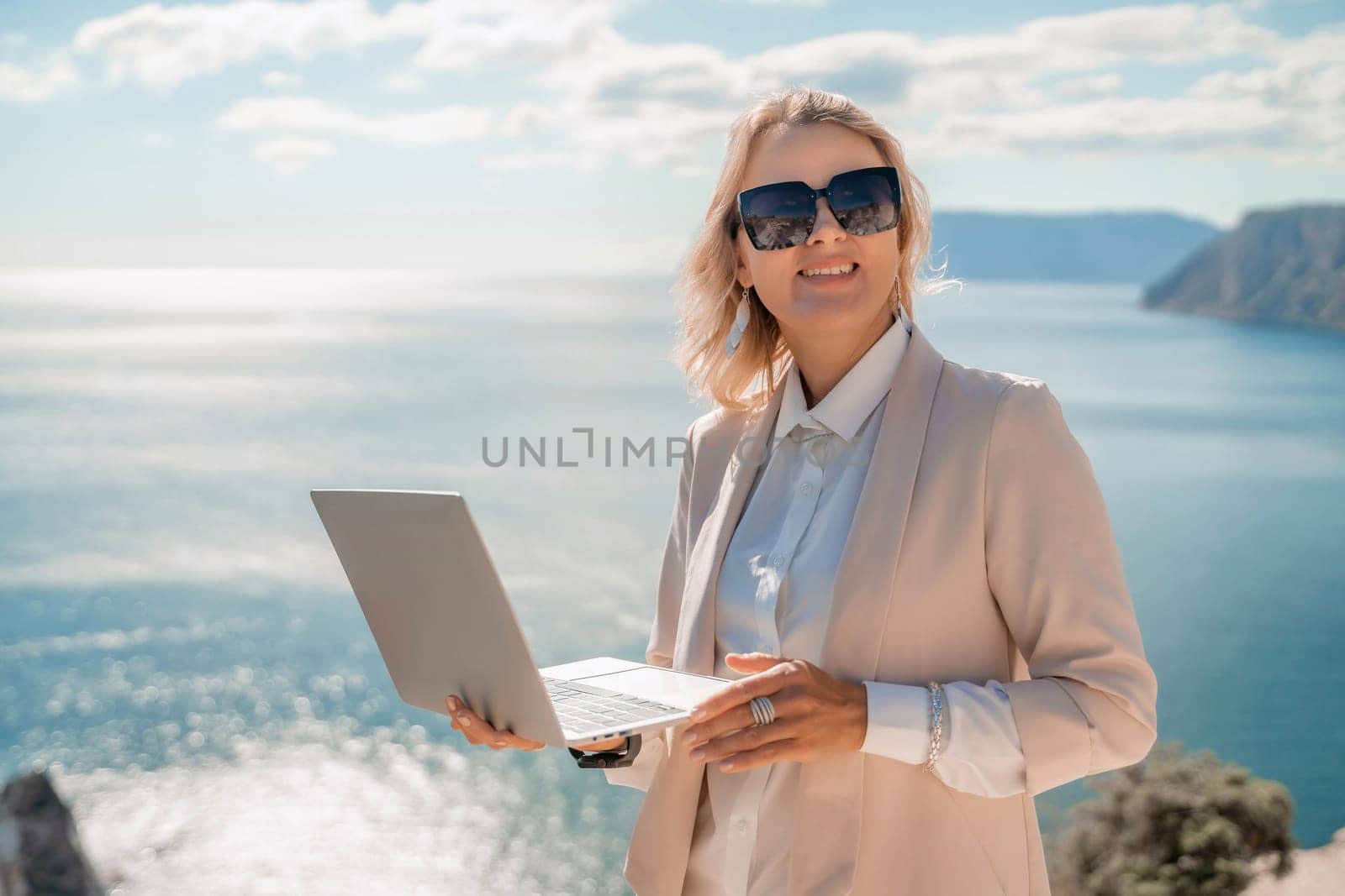 Freelance women sea. She is working on the computer. Good looking middle aged woman typing on a laptop keyboard outdoors with a beautiful sea view. The concept of remote work