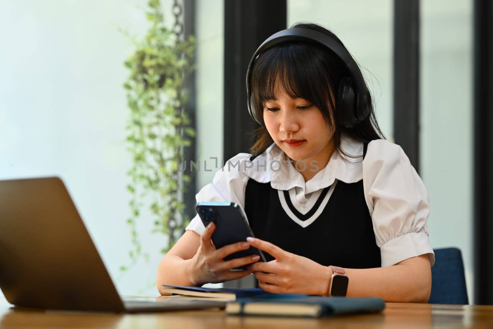 Pretty teenage asian woman listening music in wireless headphones and using smartphone.