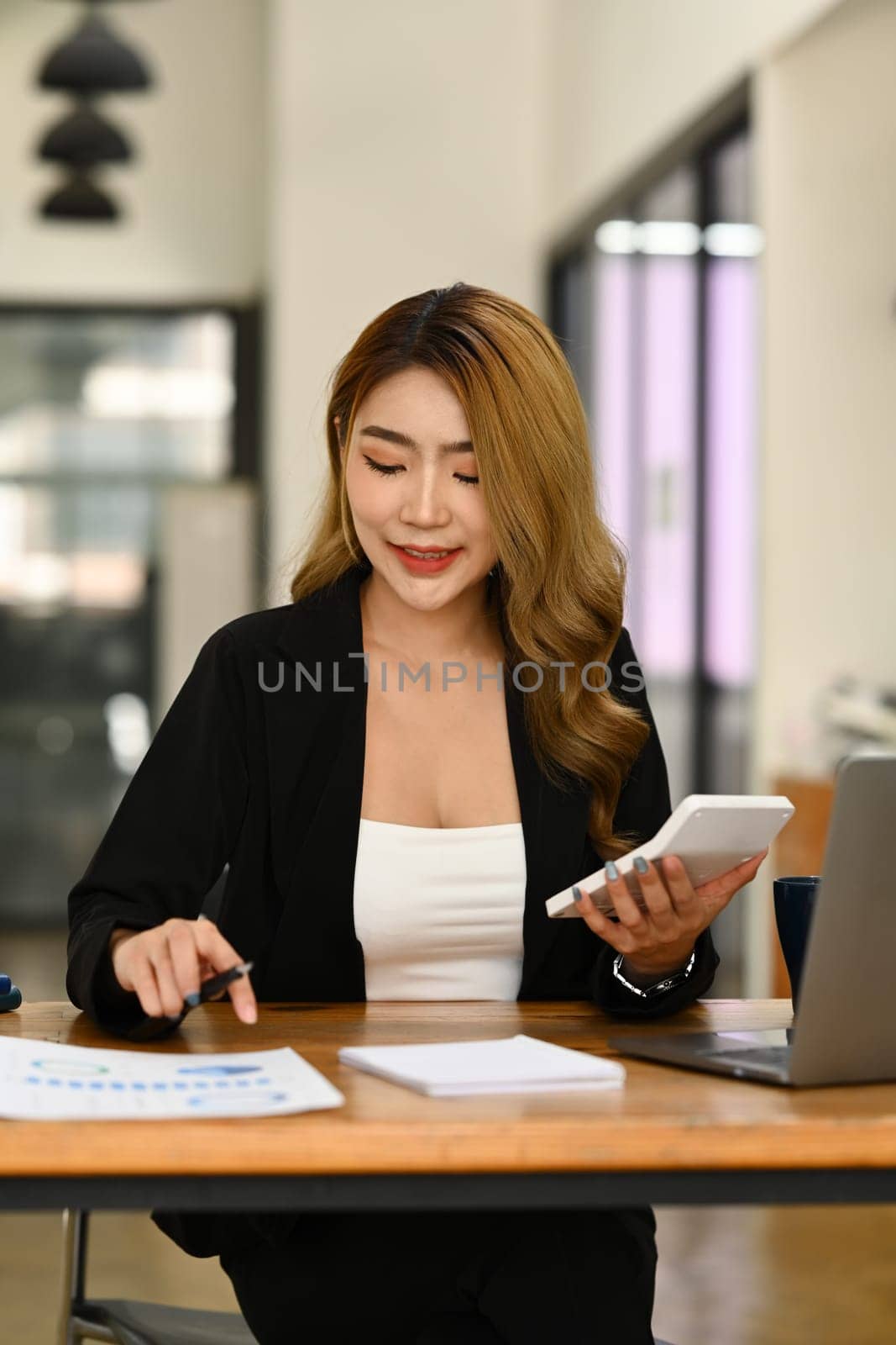 Charming asian female manager examining financial reports on wooden office desk at modern workplace.