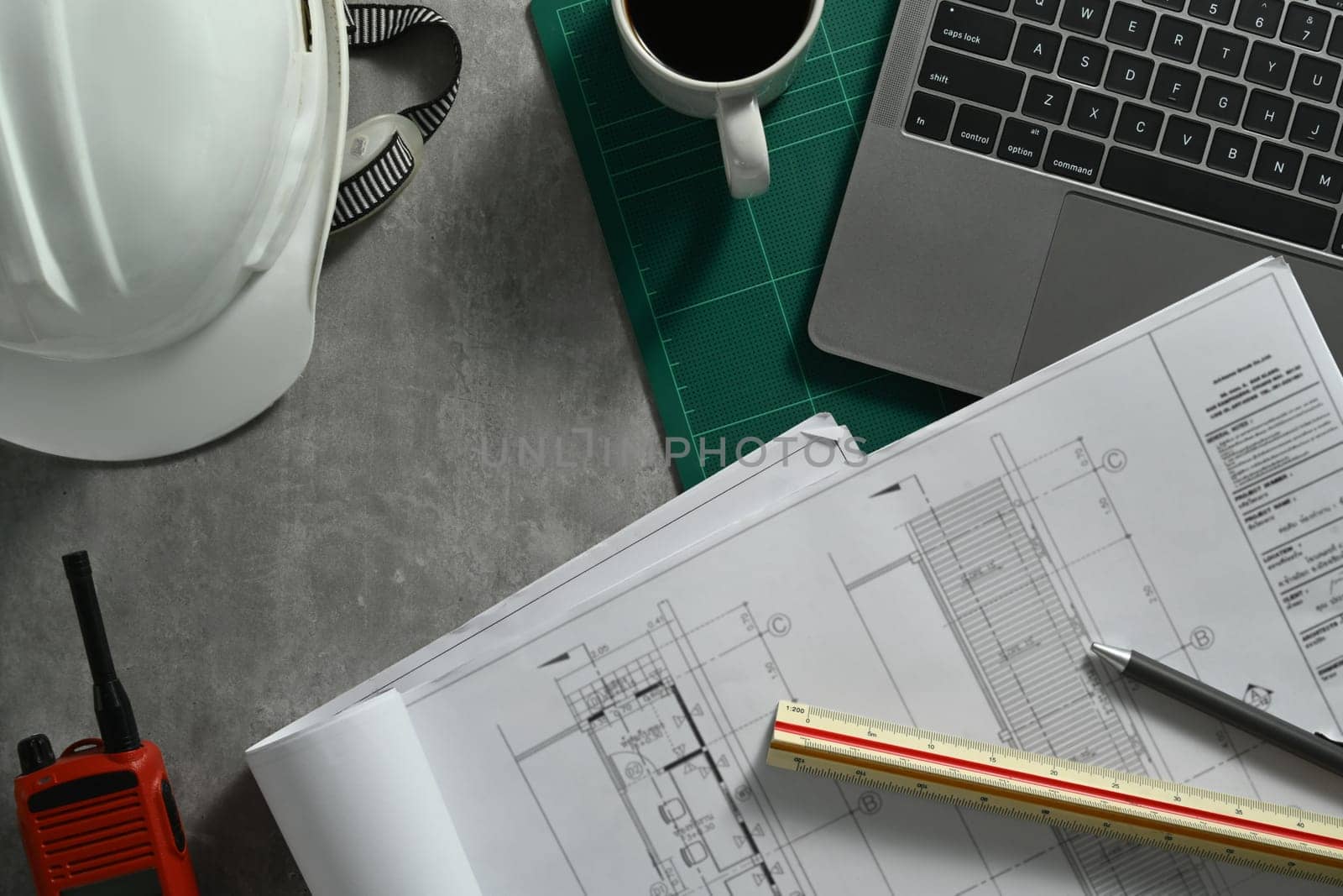 Top view of Architect workspace with laptop, safety helmet. blueprints and walkie talkie on table.