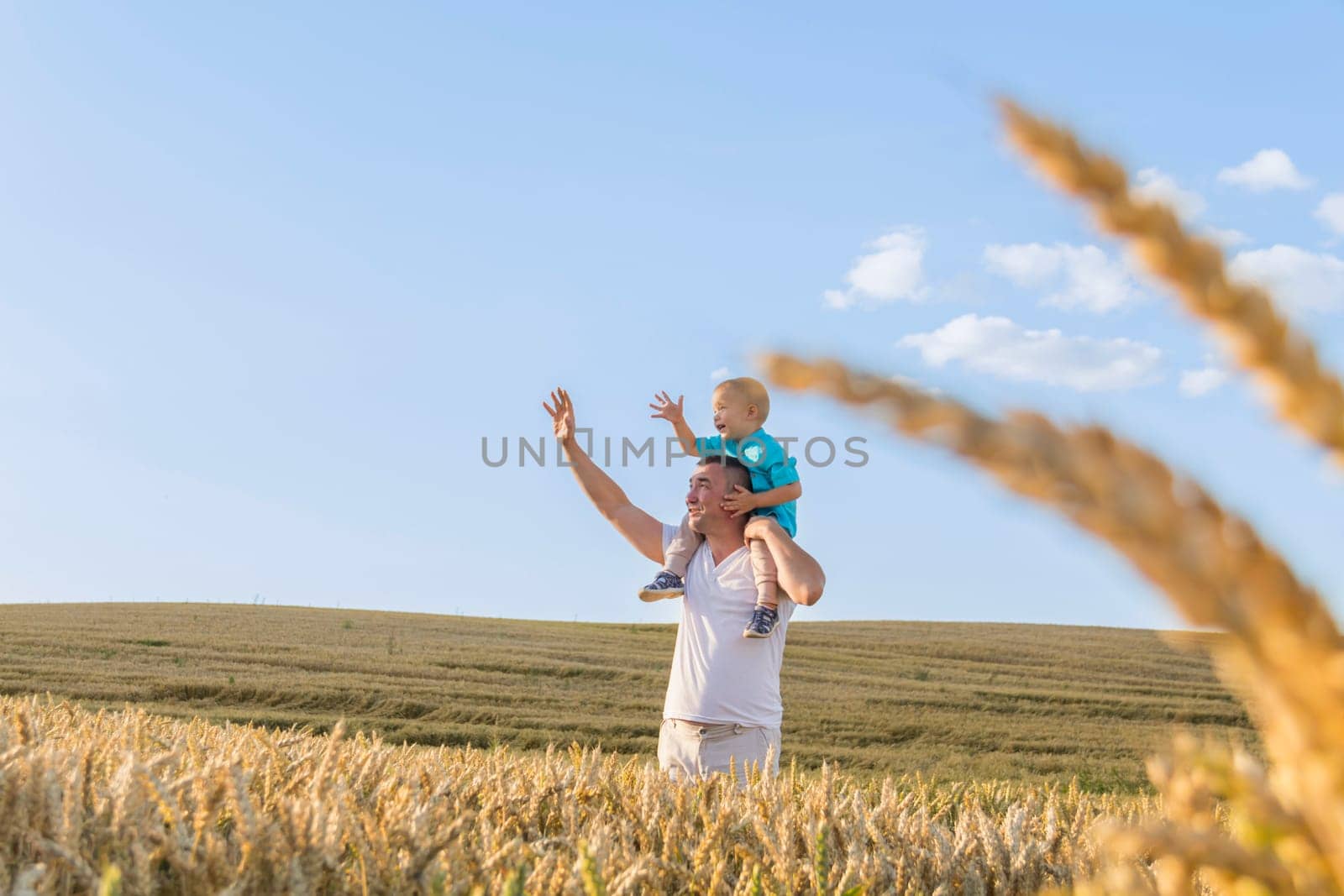 Dad and his little son are having fun walking in a field with ripe wheat. The child is sitting on the shoulders of the father. Grain for making bread. the concept of economic crisis and hunger. by Alla_Yurtayeva