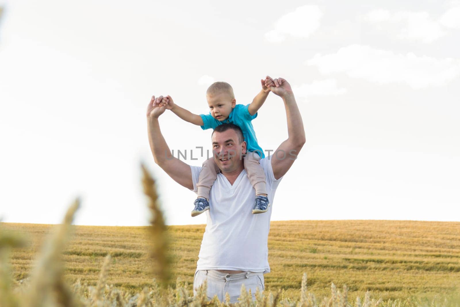 Dad and his little son are having fun walking in a field with ripe wheat. The child is sitting on the shoulders of the father. Grain for making bread. the concept of economic crisis and hunger