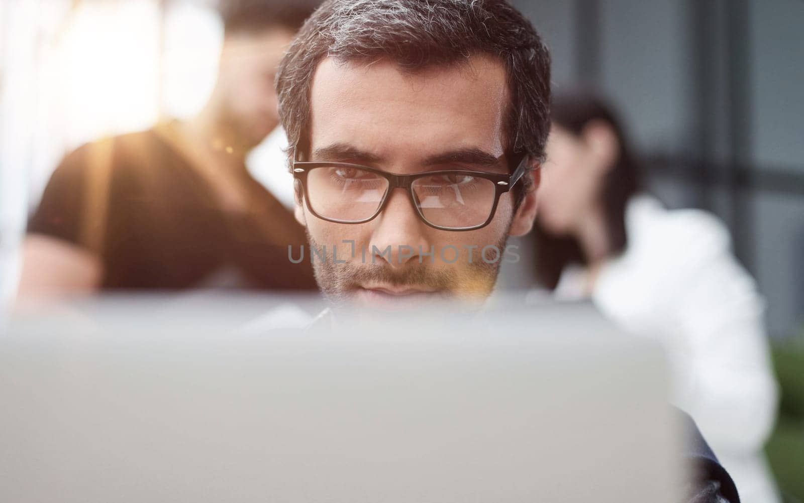 Portrait of handsome bearded man wearing glasses working with laptop in office late, his face lit up by screen by Prosto