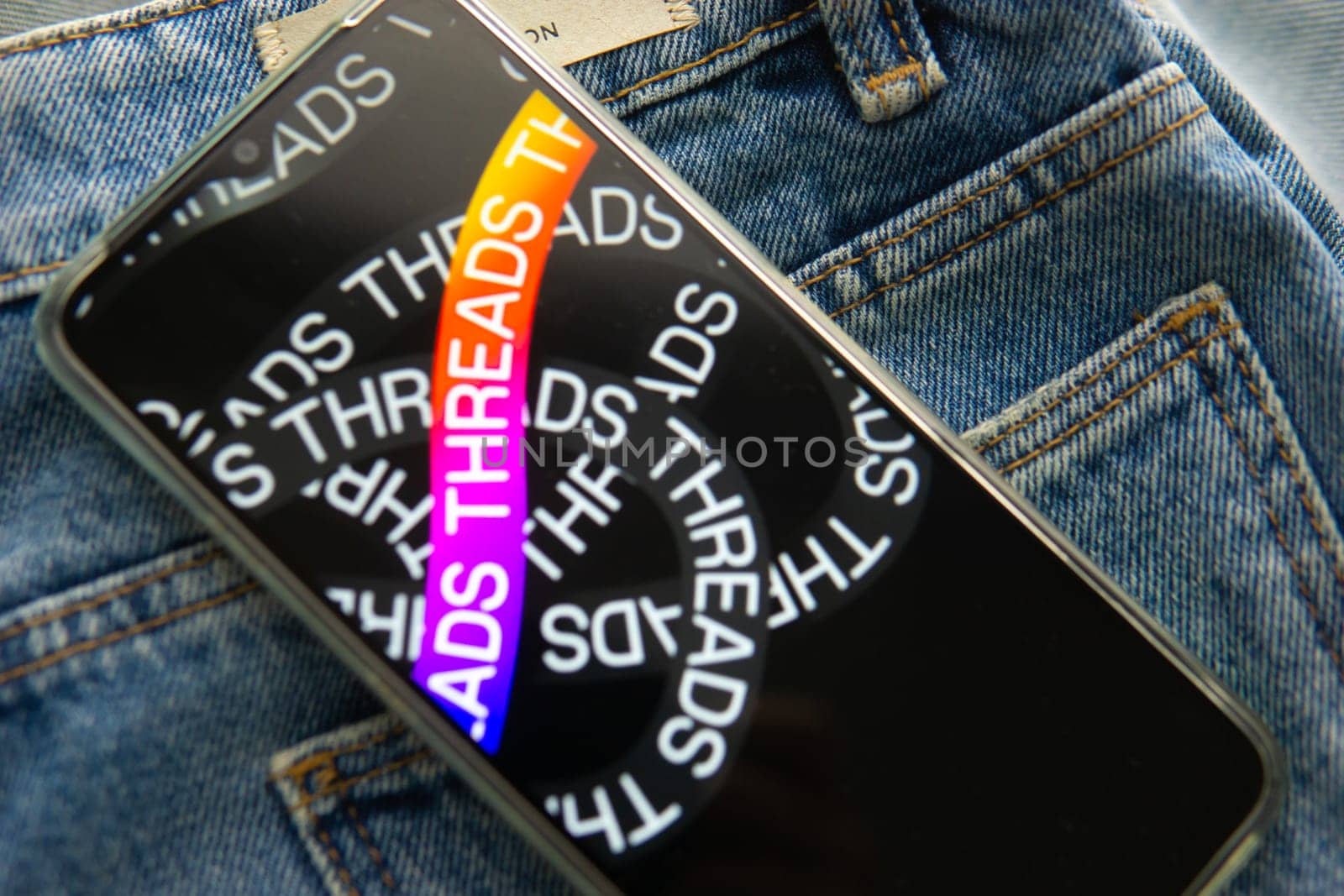 Tver, Russia - July 15, 2023, the threads logo on the smartphone screen lying on the jeans. The threads icon. The logo of the current application. Threads social network