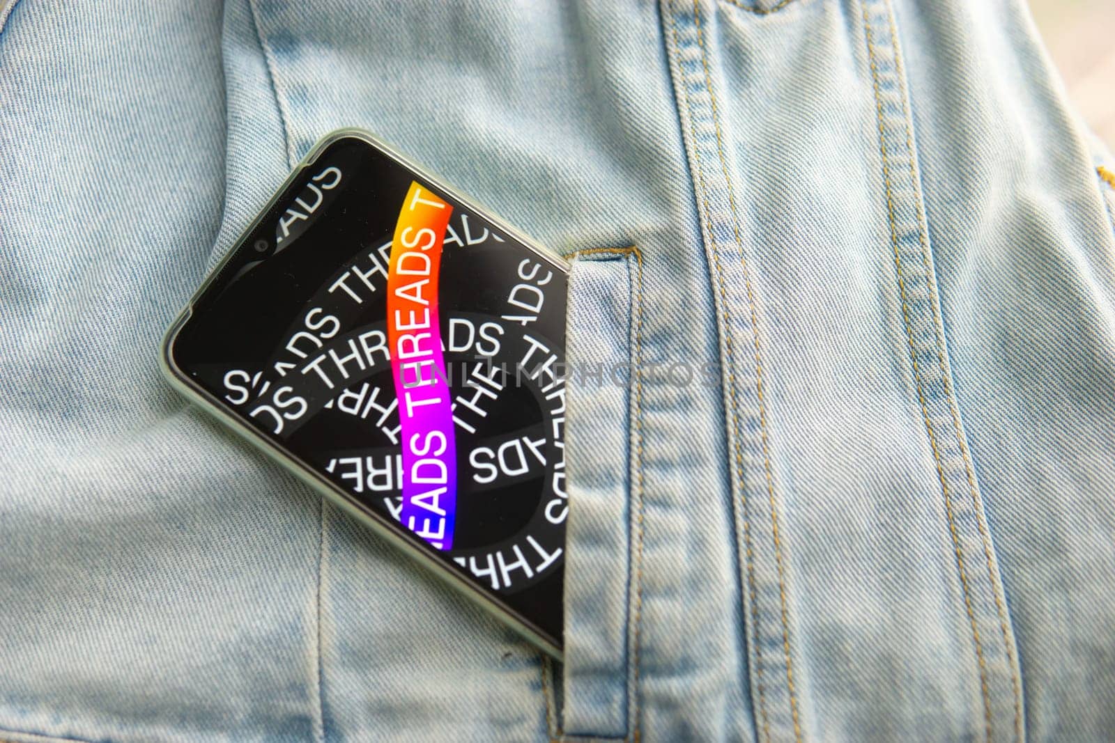 Tver, Russia - July 15, 2023, the threads logo on the smartphone screen lying on the jeans. The threads icon. The logo of the current application. Threads social network