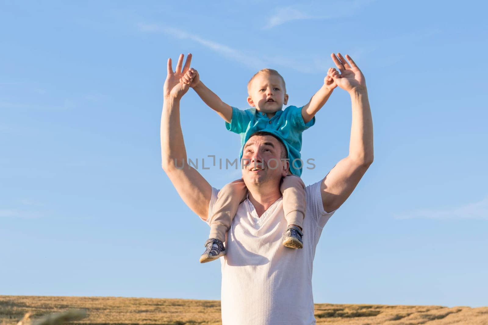 Dad and his little son are having fun walking in a field with ripe wheat. The child is sitting on the shoulders of the father. Grain for making bread. the concept of economic crisis and hunger