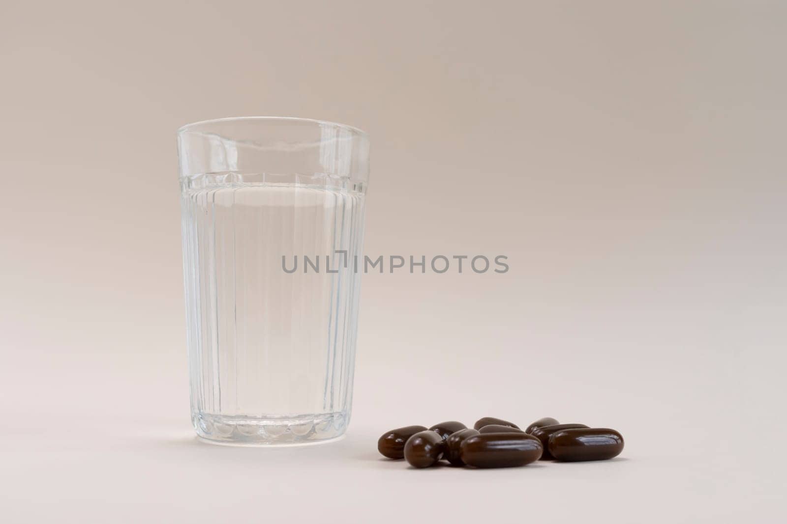 Selective Focus Lying Scattered Brown Sunflower Lecithin Softgel Pill Capsules And Glass Of Water On Beige Background. Dietary Supplements, Vitamins. Copy Space For Text. Healthy Lifestyle Horizontal.