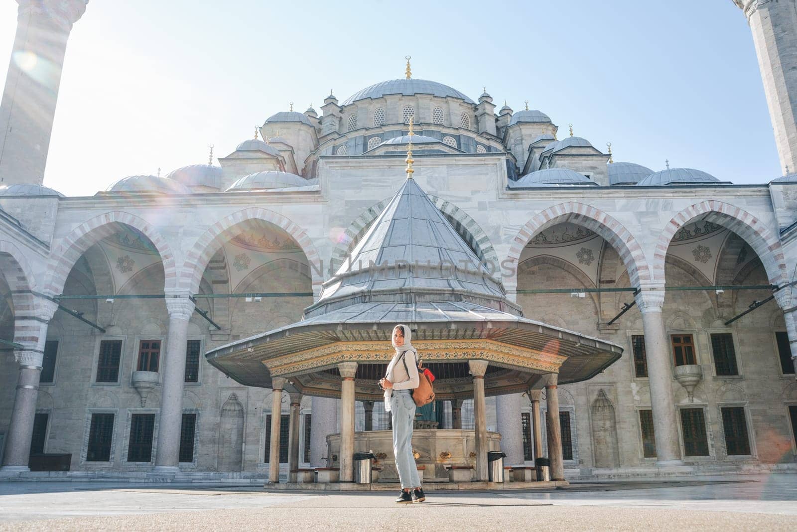 A young female traveler with a backpack on her back walks towards the Fatih Mosque in Istanbul by Ekaterina34