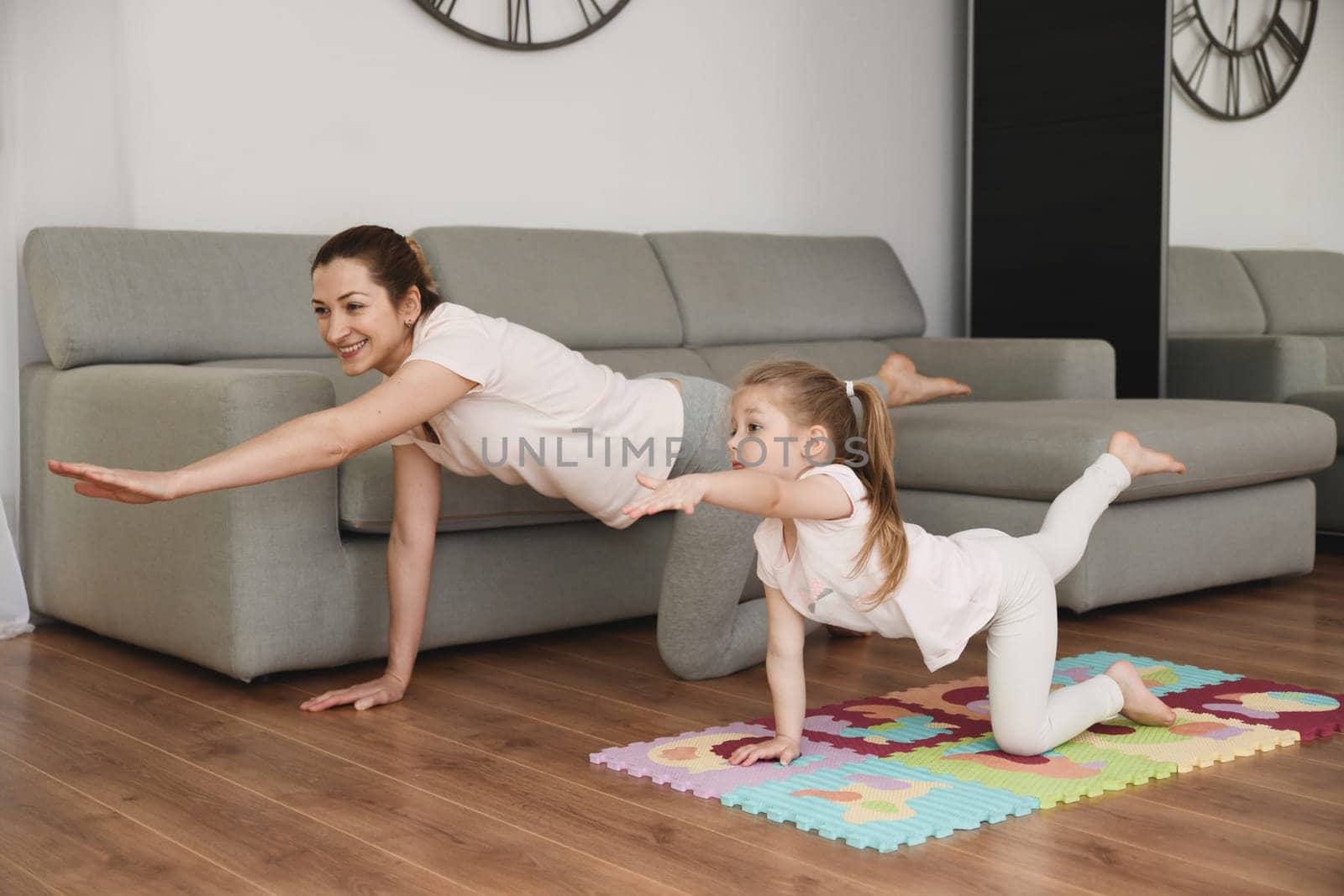 Mother and daughter doing yoga at home. by Godi