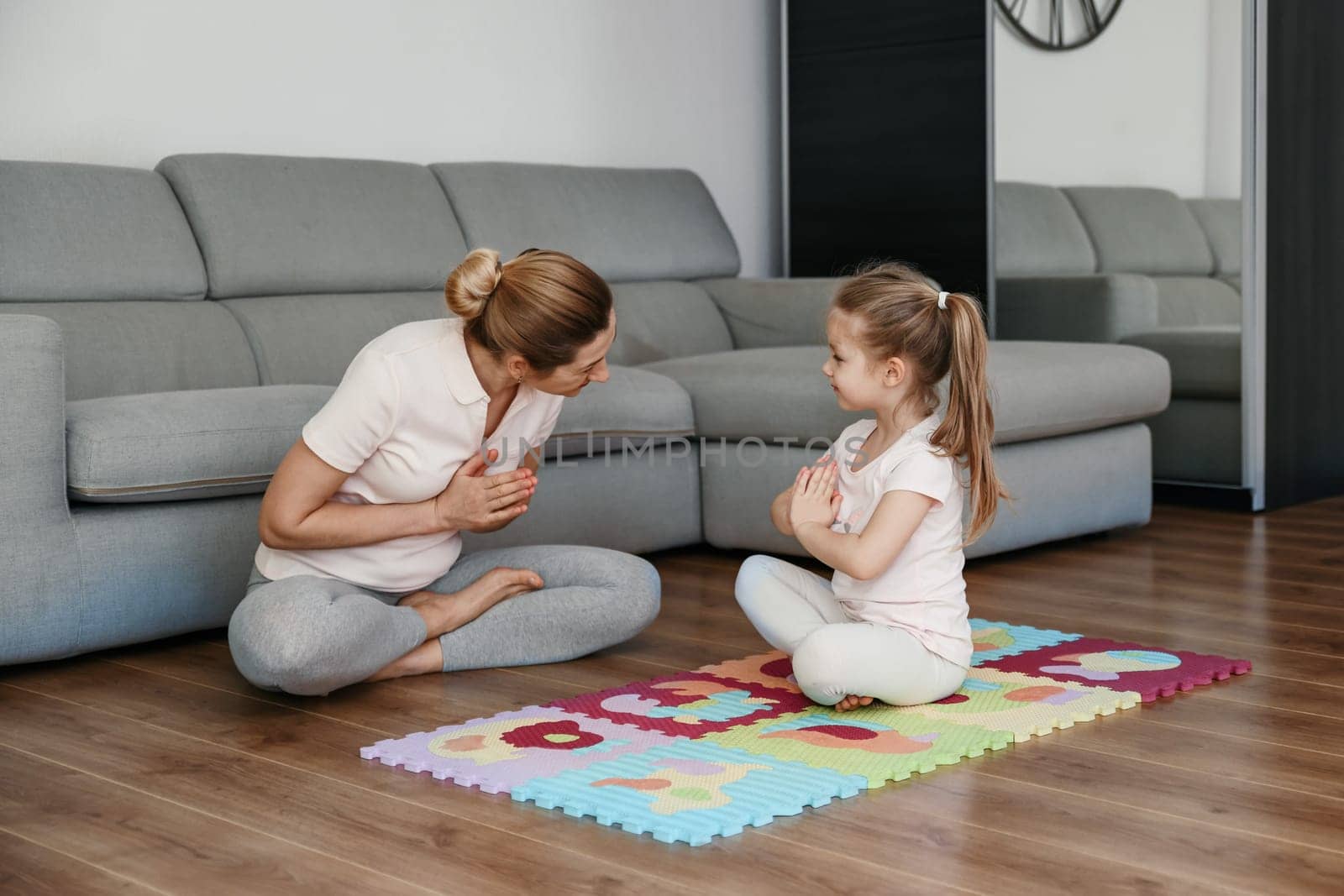 Mother and daughter doing yoga at home. by Godi